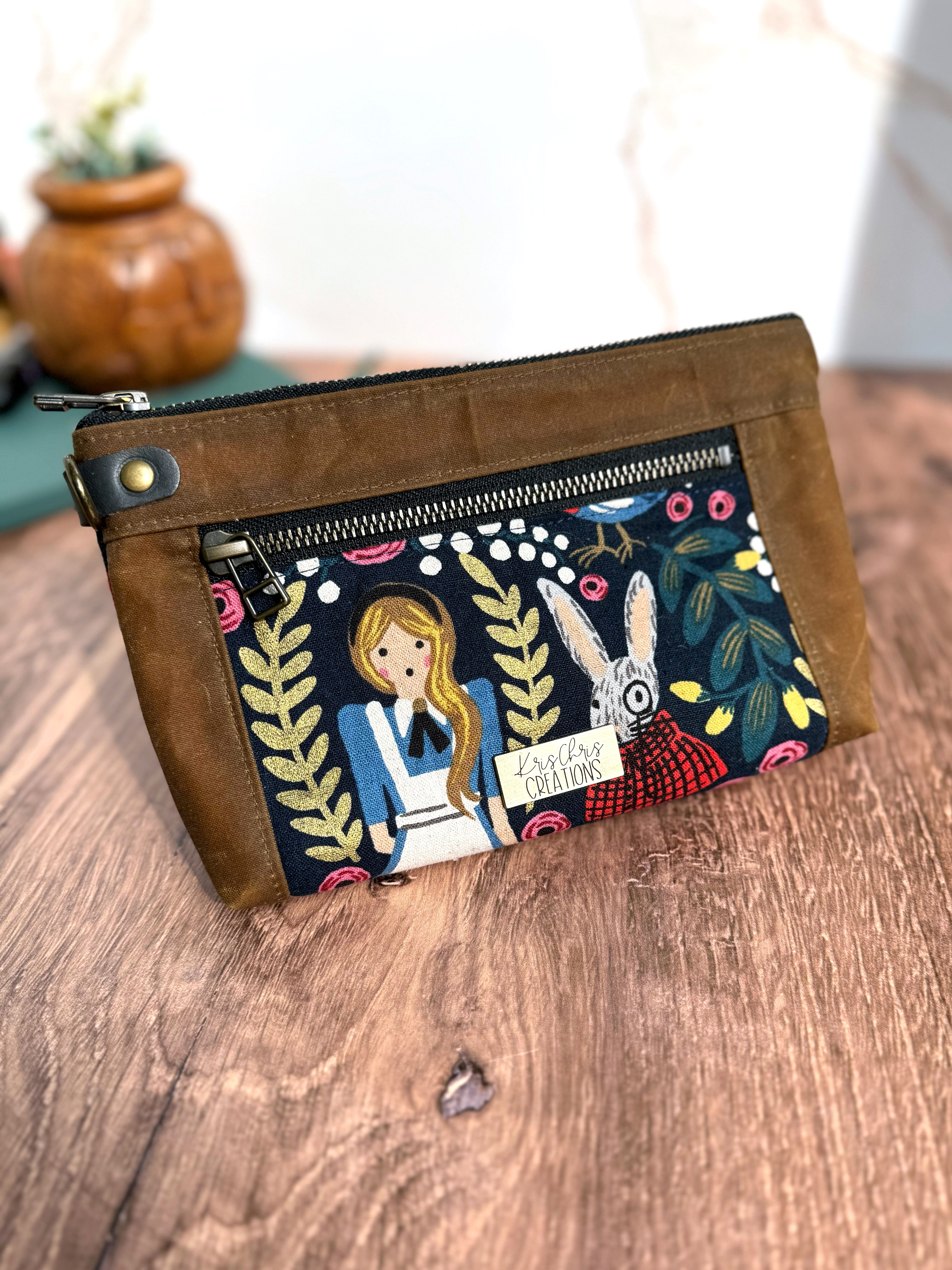 Alice in Wonderland pouch showing Alice and the rabbit. 2 zippers break up the brown waxed canvas trim.
