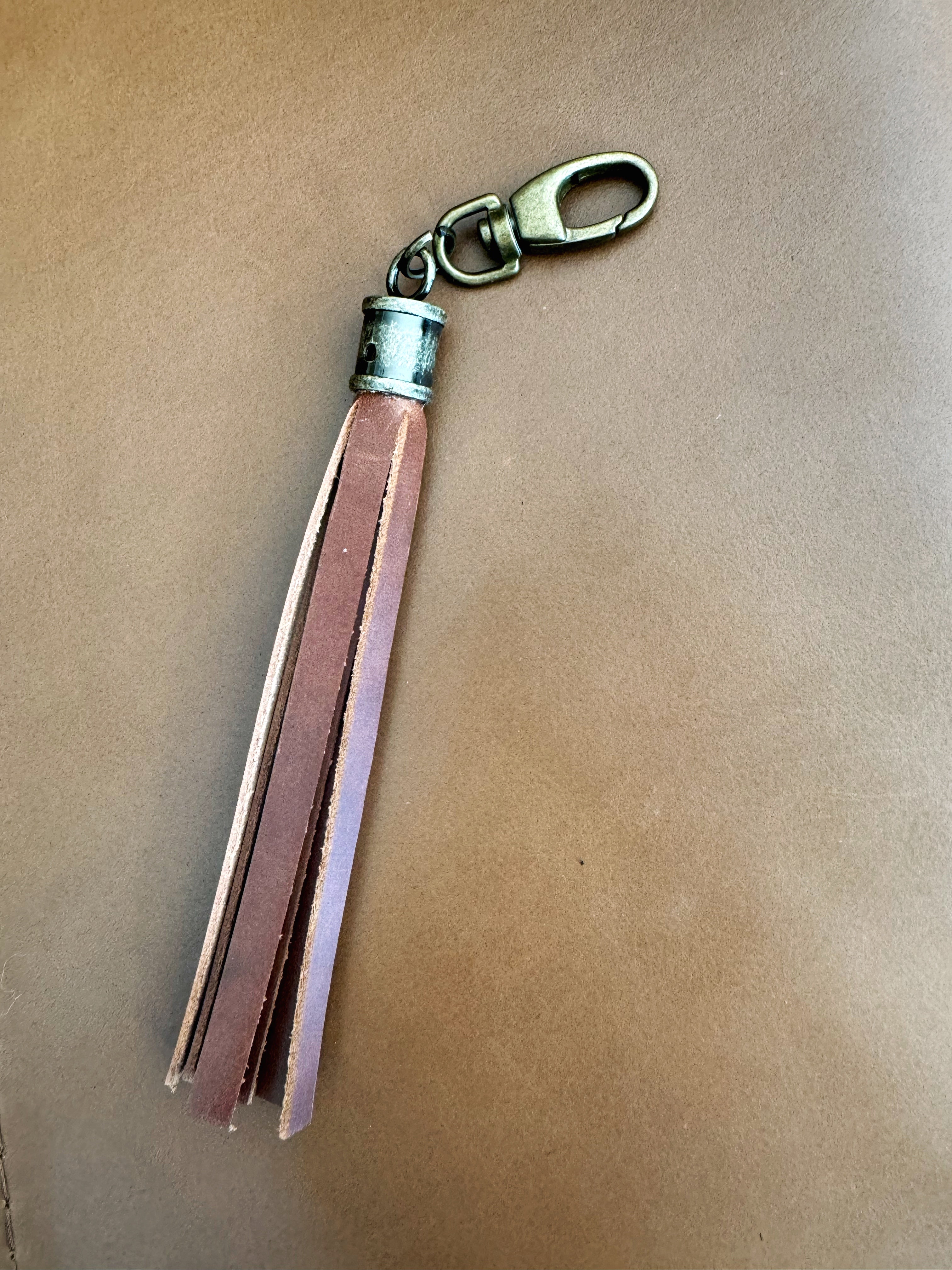 Tassel with brown leather fringe and cylindrical antique brass hardware. Lobster clasp easily attaches to bags and accessories.