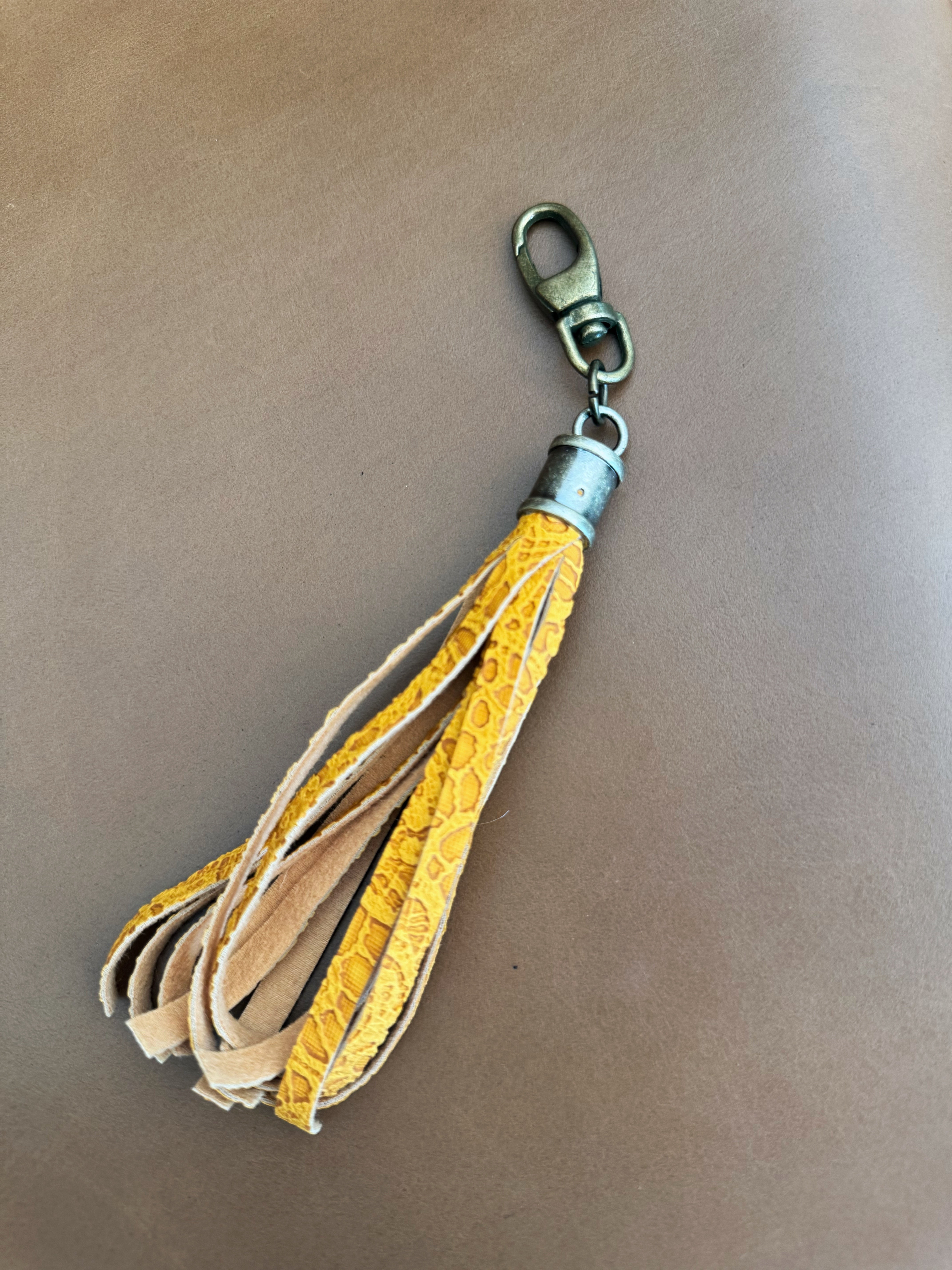 Tassel with yellow lace vinyl fringe and cylindrical antique brass Hardware. Lobster clasp easily attaches to bags and accessories.