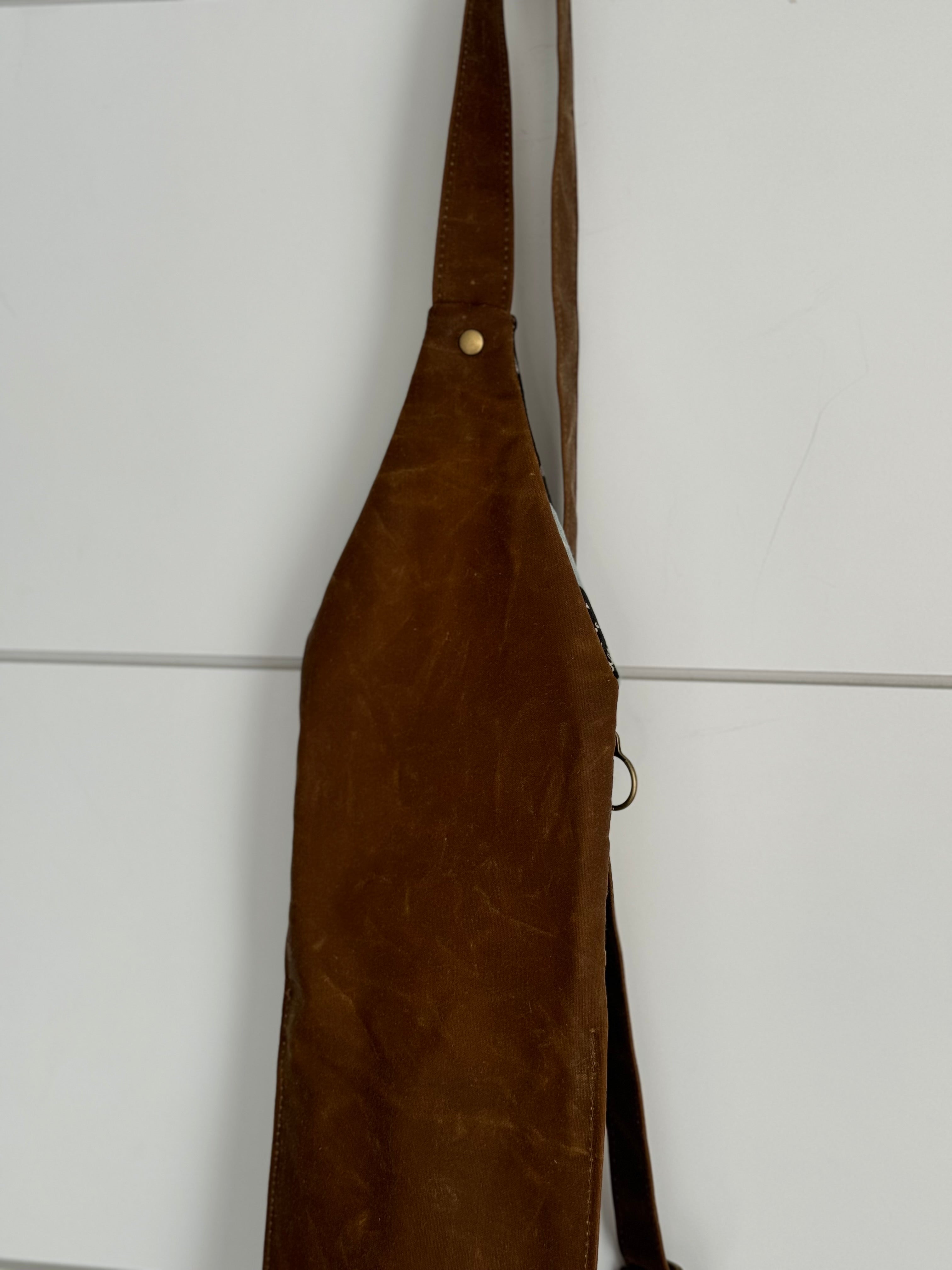 Back side of crossbody bag hanging with white background. In brown solid waxed canvas.