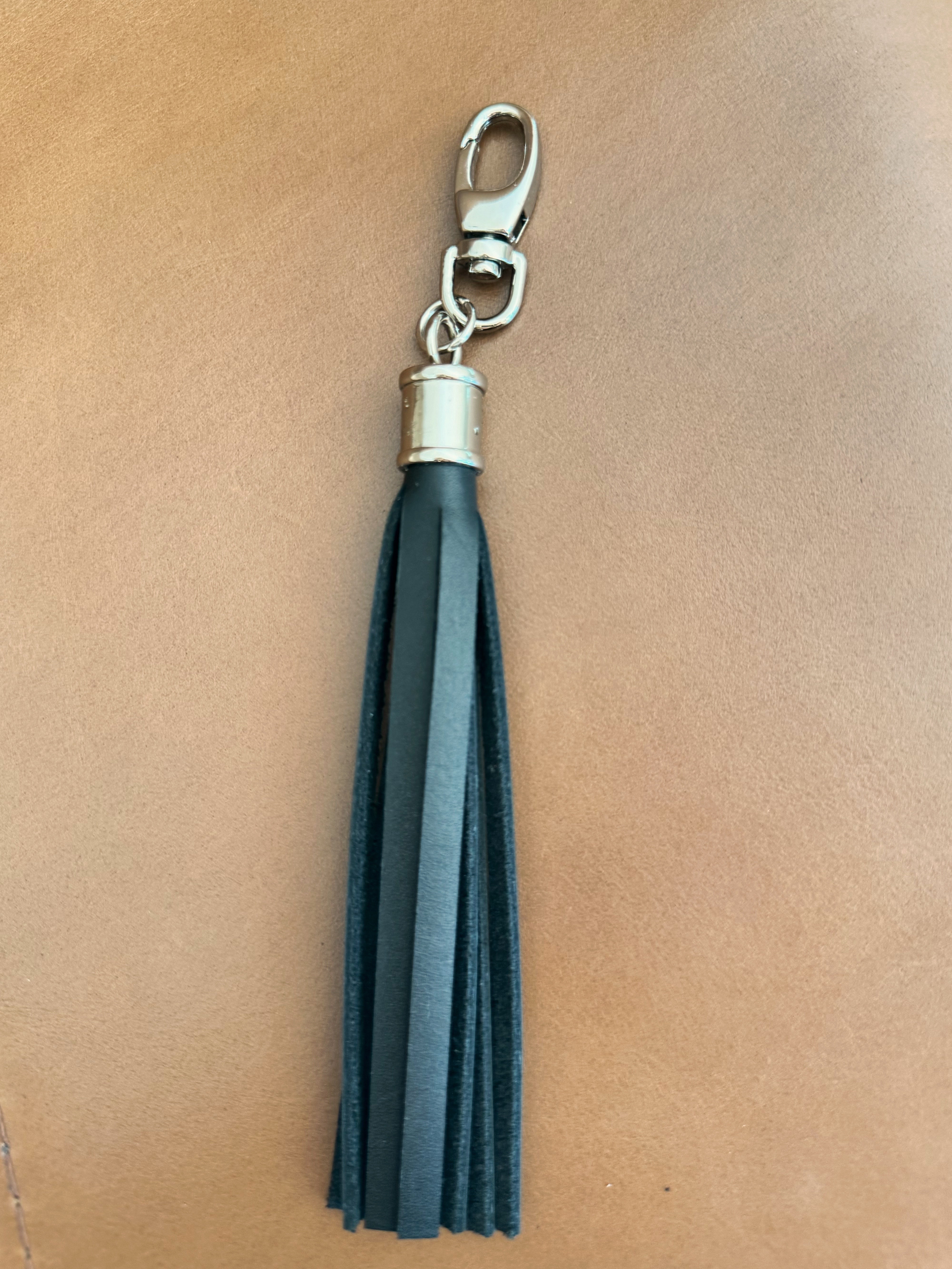 Tassel with black leather fringe and cylindrical nickel hardware. Lobster clasp easily attaches to bags and accessories.