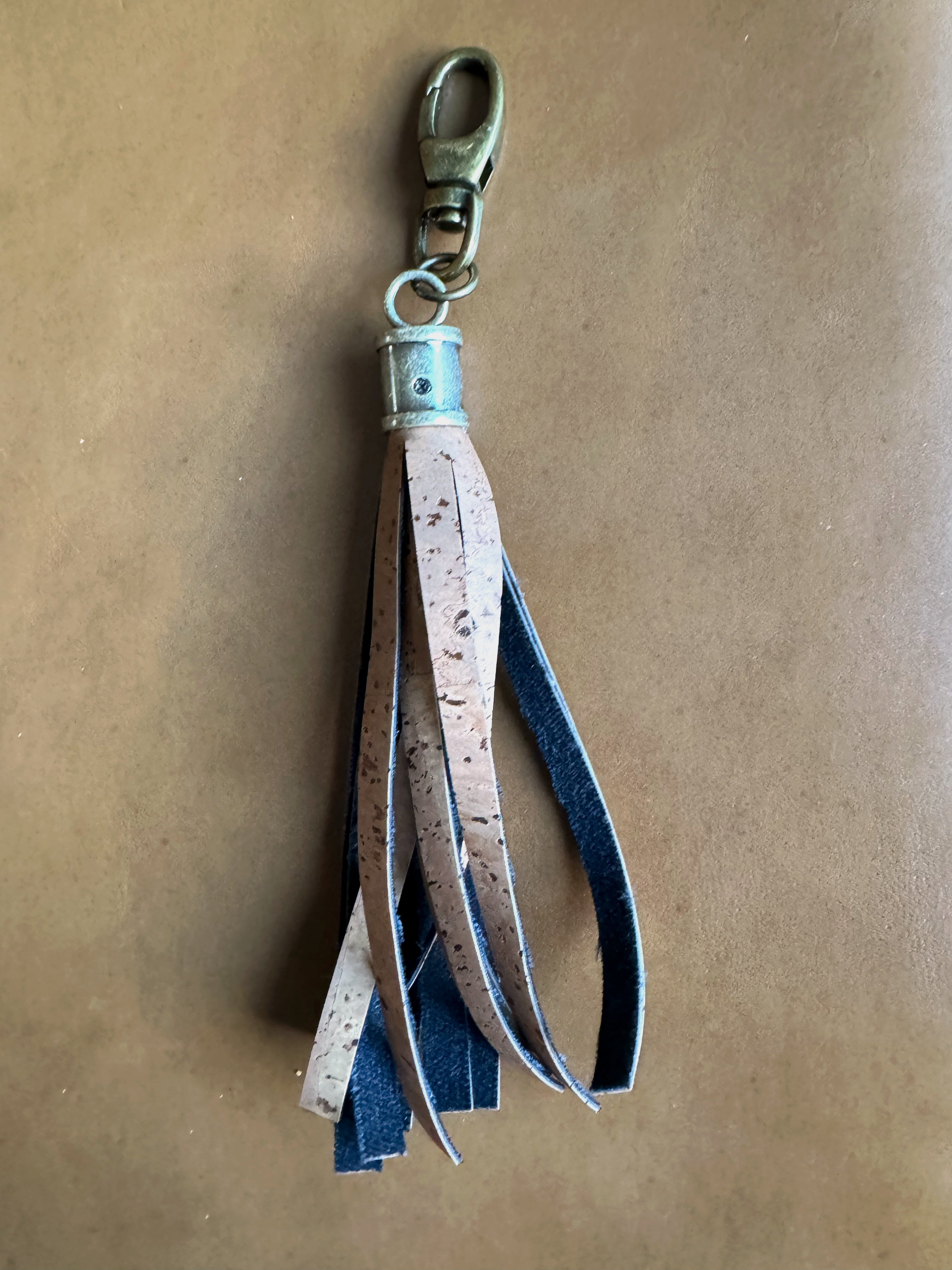 Tassel made from brown cork fabric and cylindrical antique brass hardware. Lobster clasp easily attaches to bags and accessories.