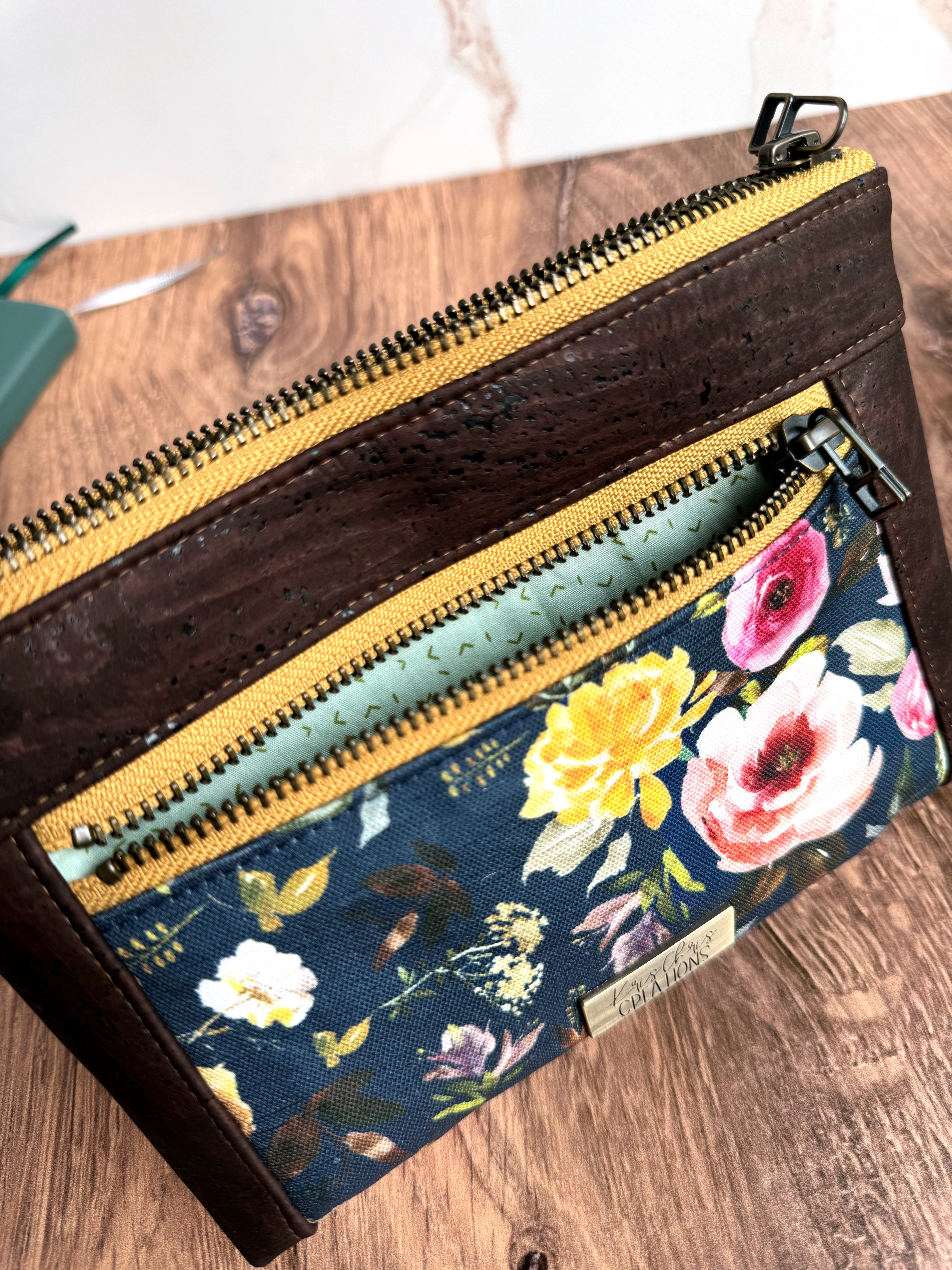 Floral pouch shows light teal lining fabric in small zipper pocket on wooden base and white marble backgr