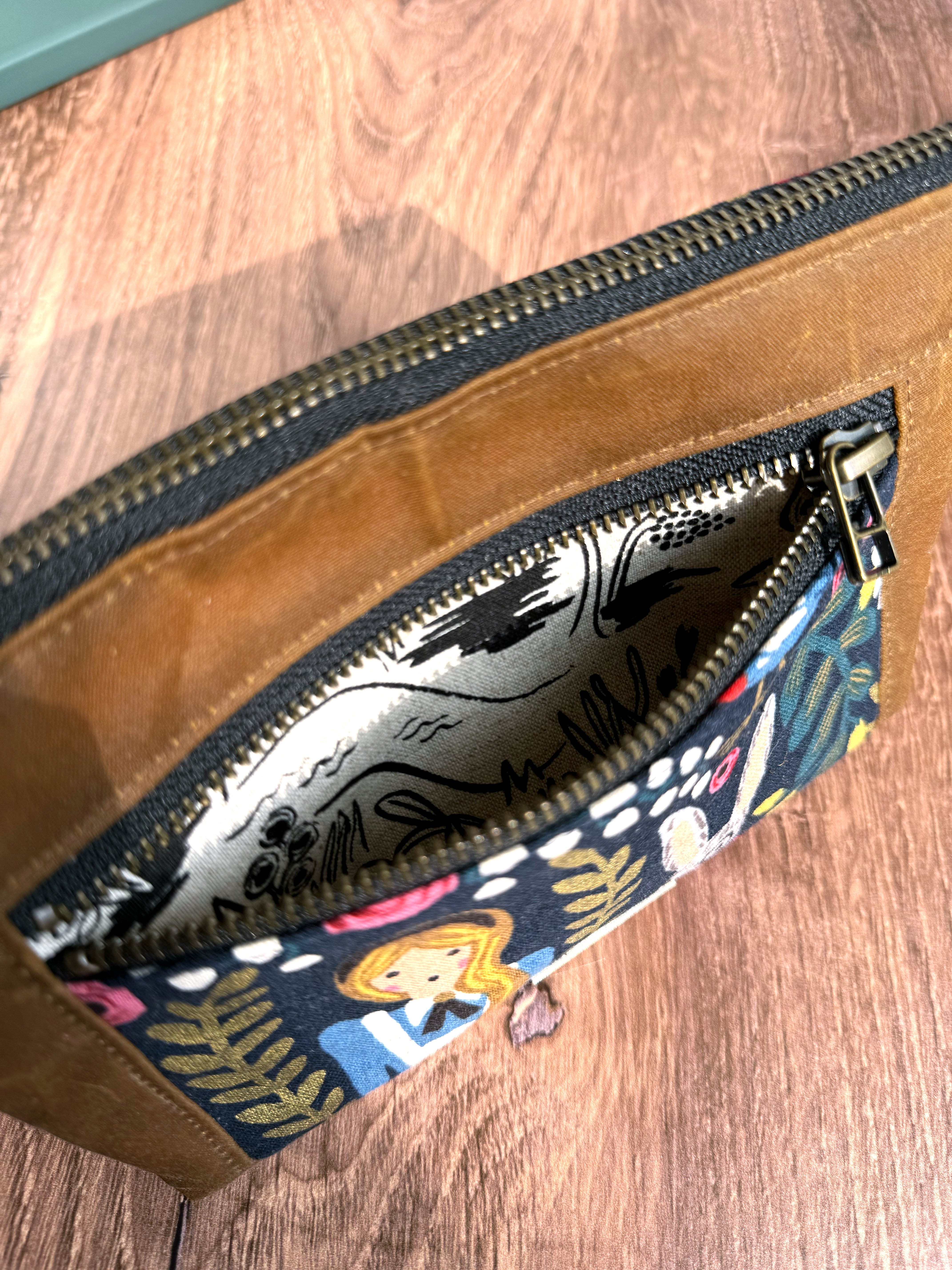 Open zipper on Alice in Wonderland pouch shows black and white lining fabric - more Alice themed canvas illustrations.