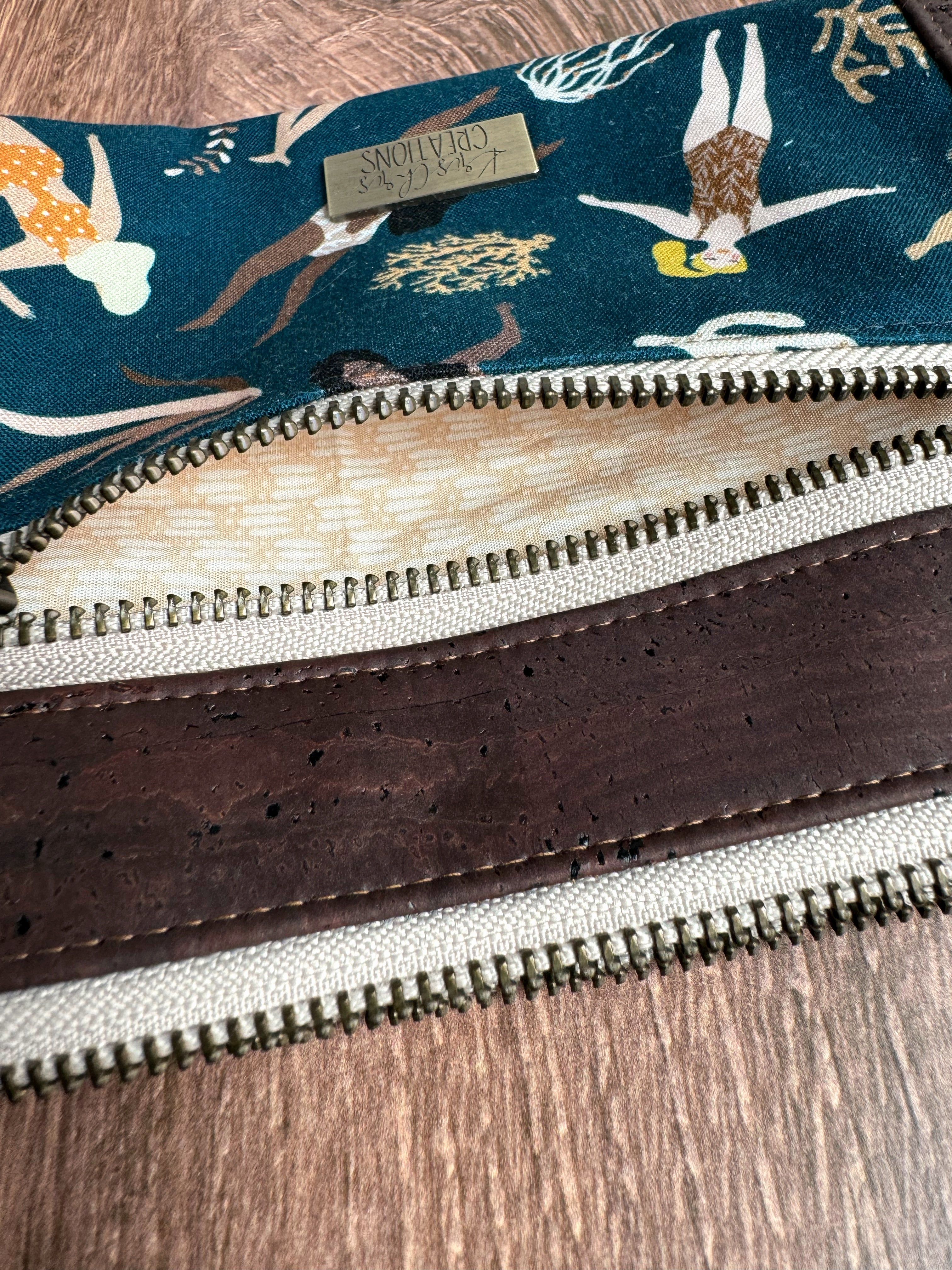 Small open brass zipper shows creamy tan interior fabric and close up of brown cork trim