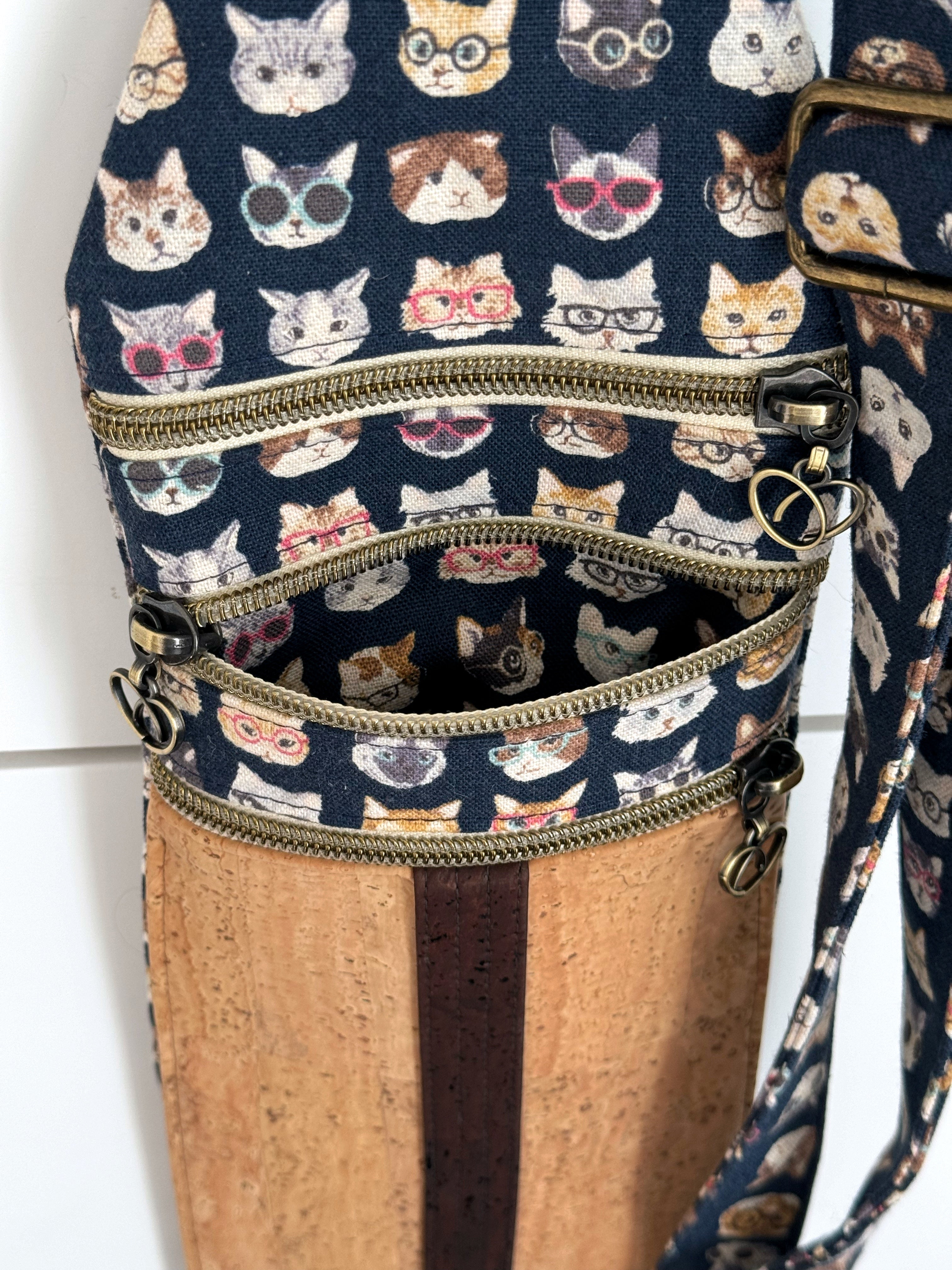 Bag featuring cats wearing glasses has 3 antique brass zippers. Middle zipper (of 3) is opened showing cat lining inside.