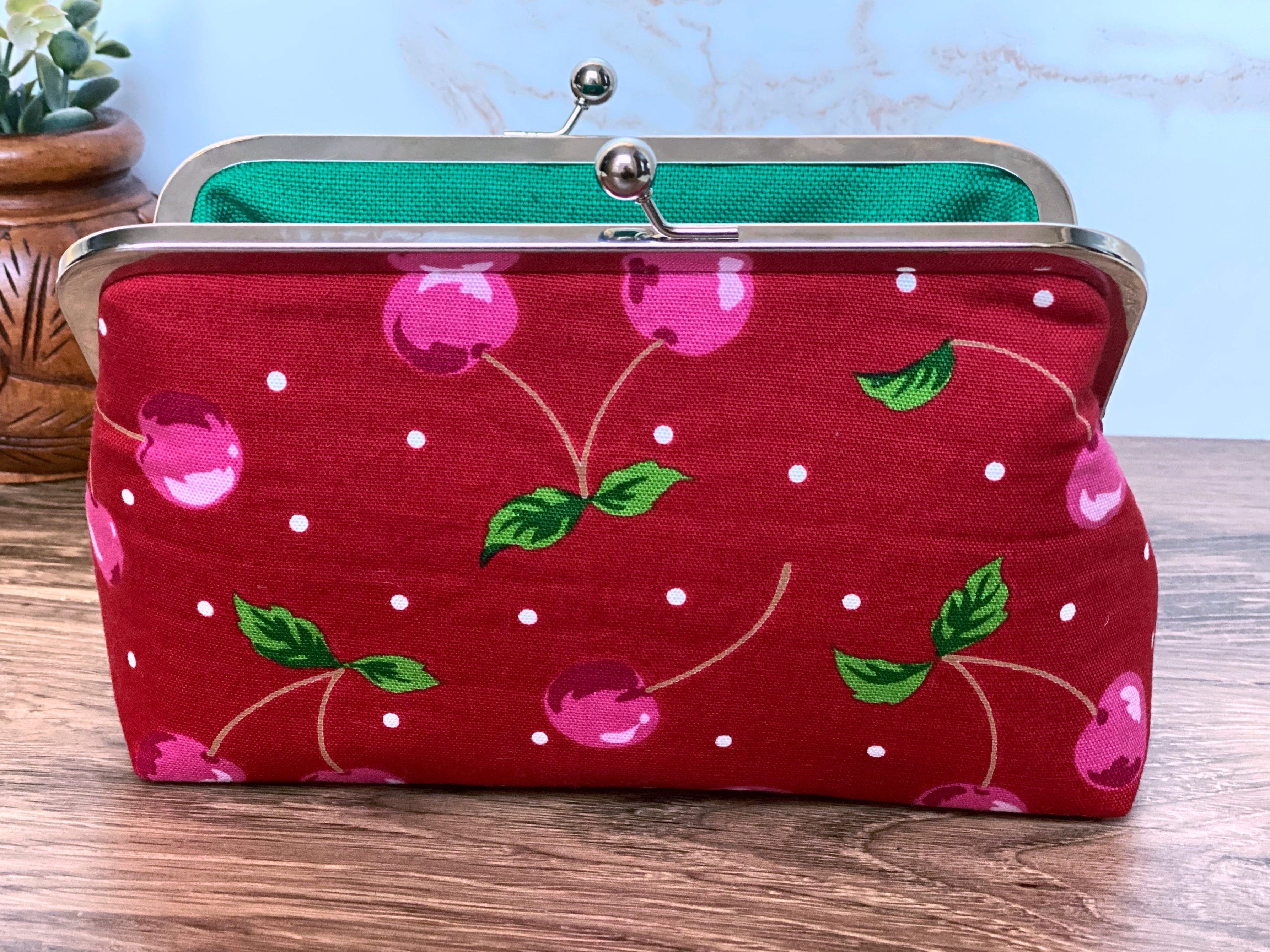 Close view of Cherry kisslock clutch bag showing bright red canvas fabric, pink cherries, and green leaves.