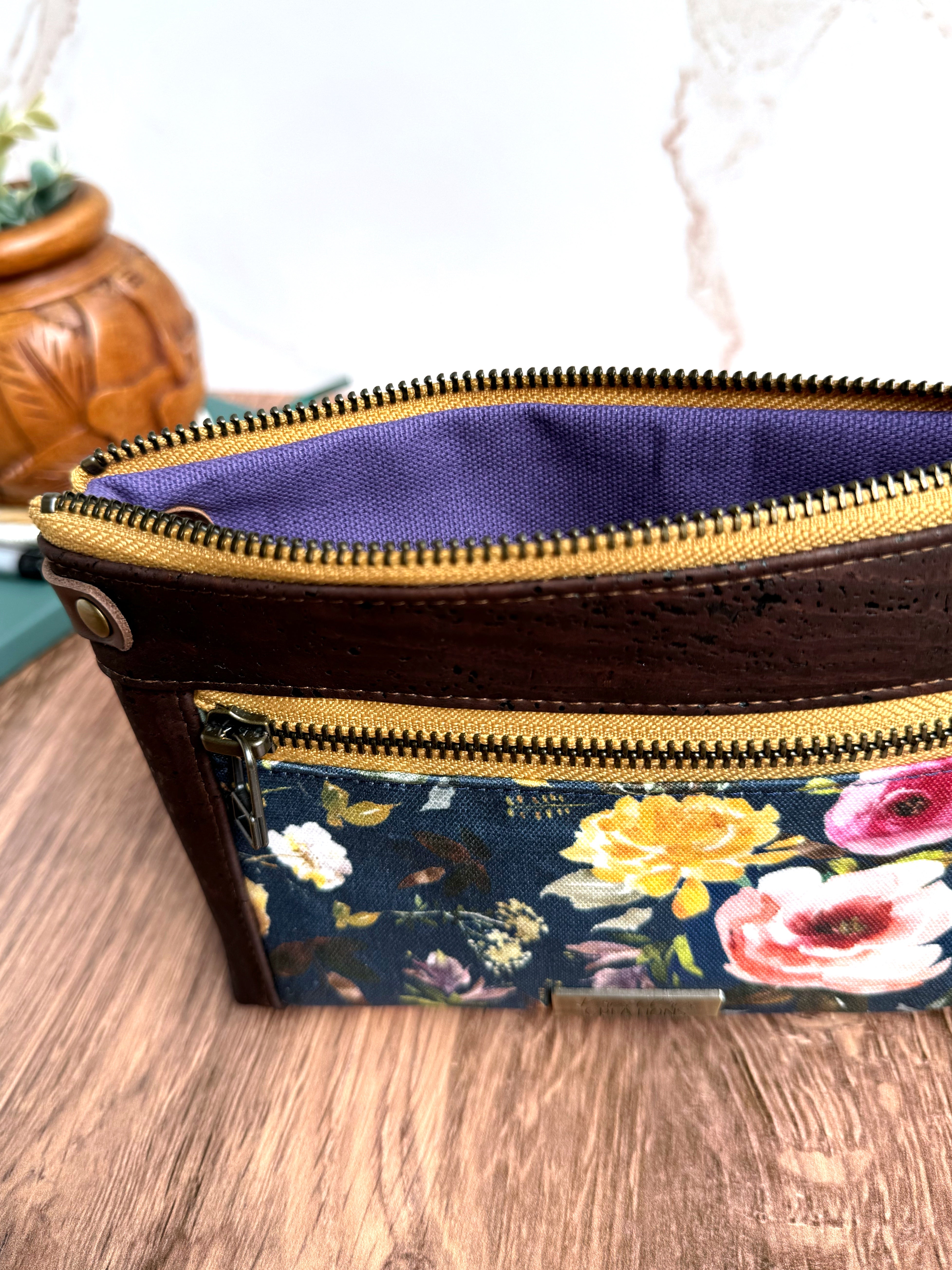 Floral pouch is open to show purple lining fabric with wooden flooring.