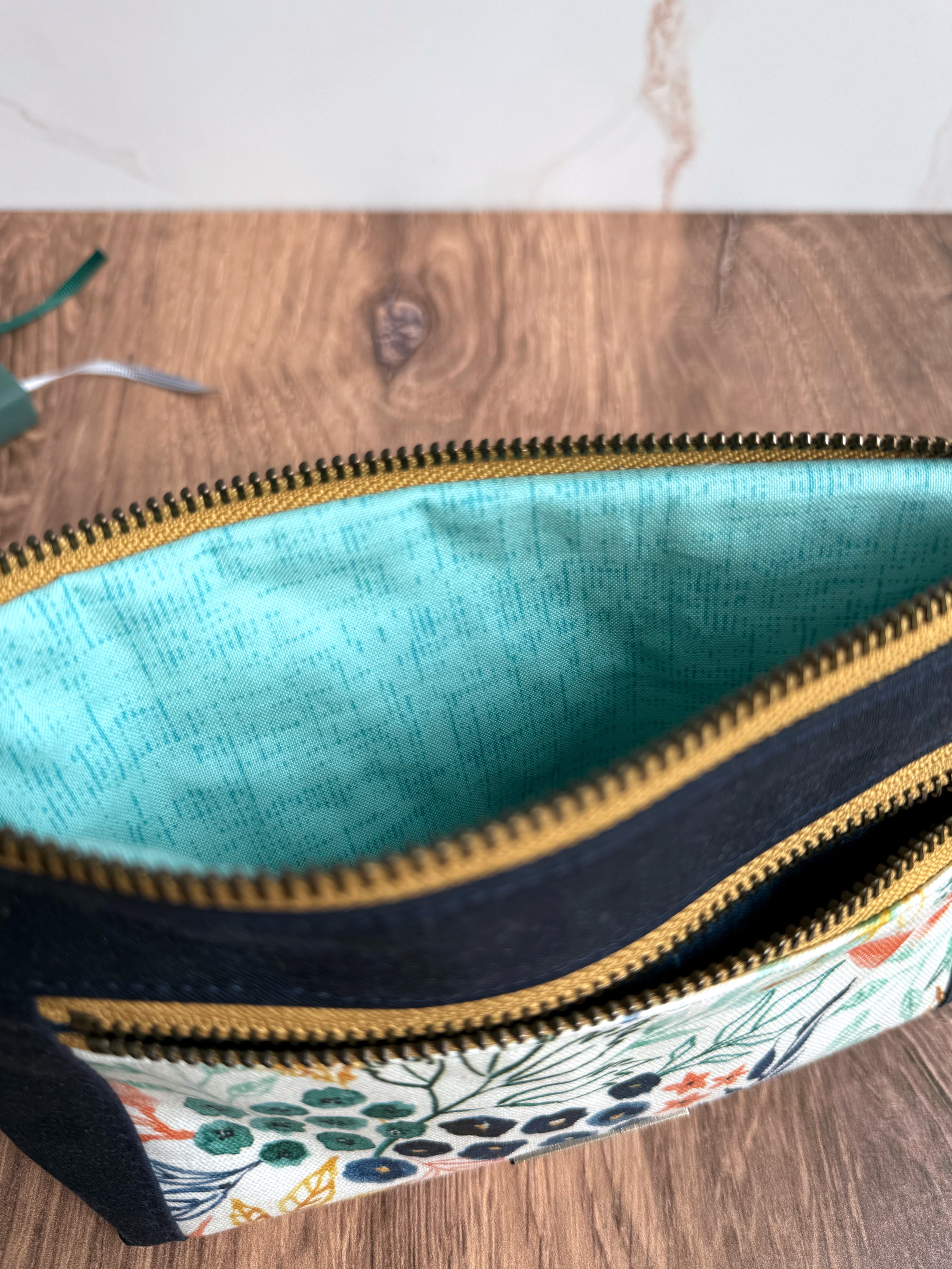 Open zipper shows light teal lining inside pouch with wooden flooring.
