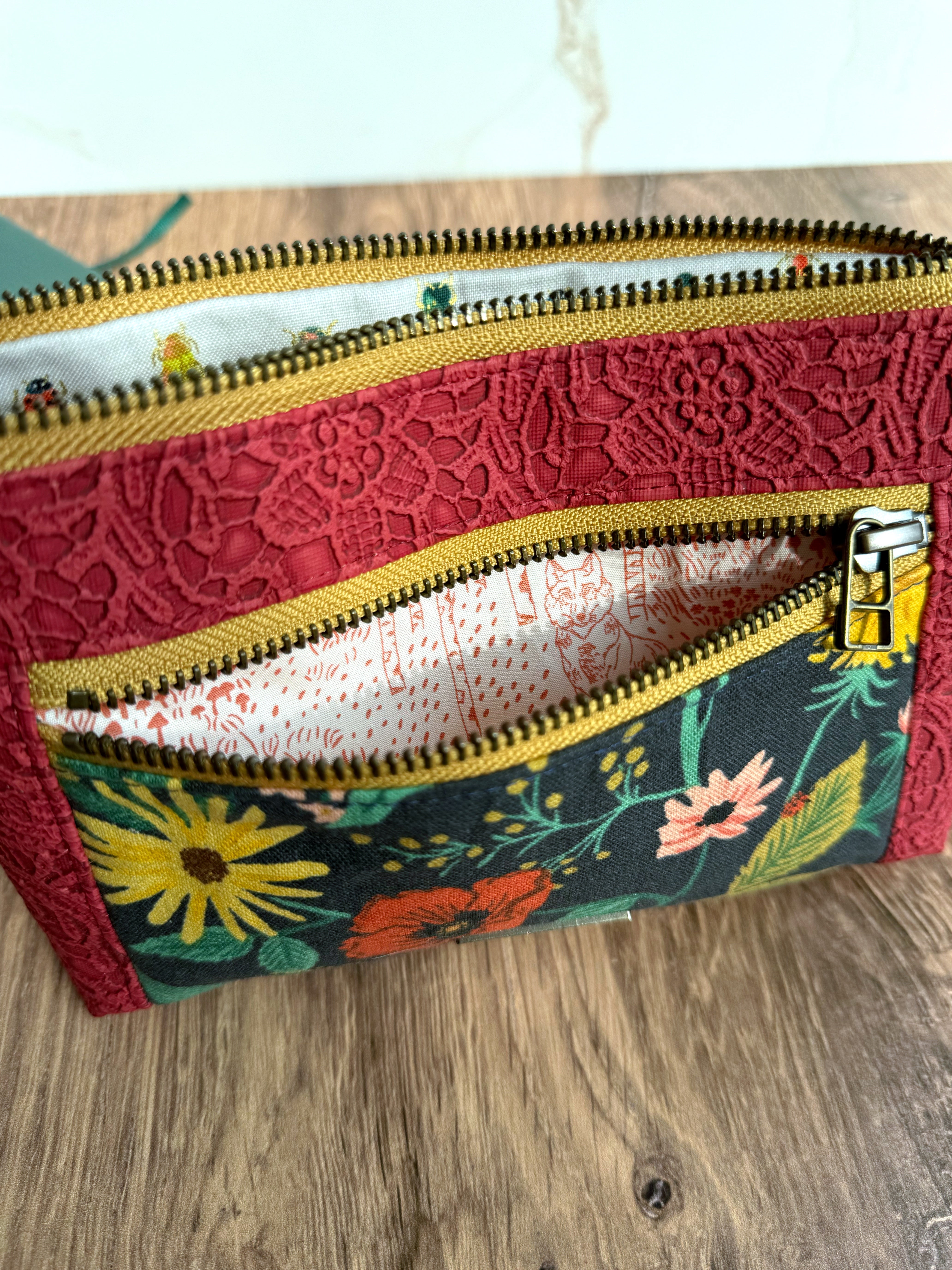 Floral pouch shows different illustrated fabrics inside zipper pockets. Colors of yellow zipper trim, red lace vinyl, and Rifle Paper Co. canvas contrast.