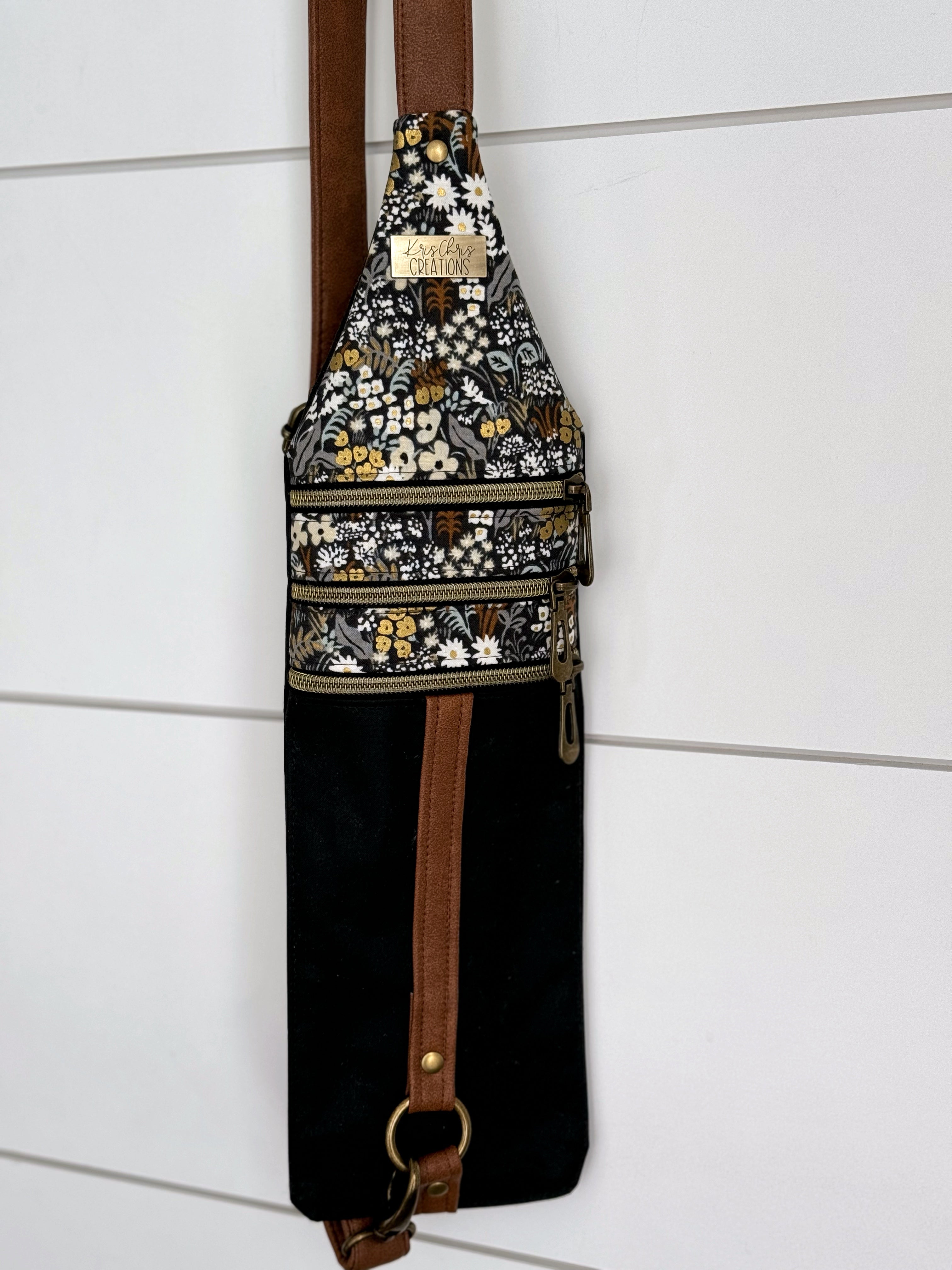 Full view of Crossbody bag shows Floral fabrics on top, 3 brass zippers, and brown vinyl adjustable straps extending from top of back to the bottom.