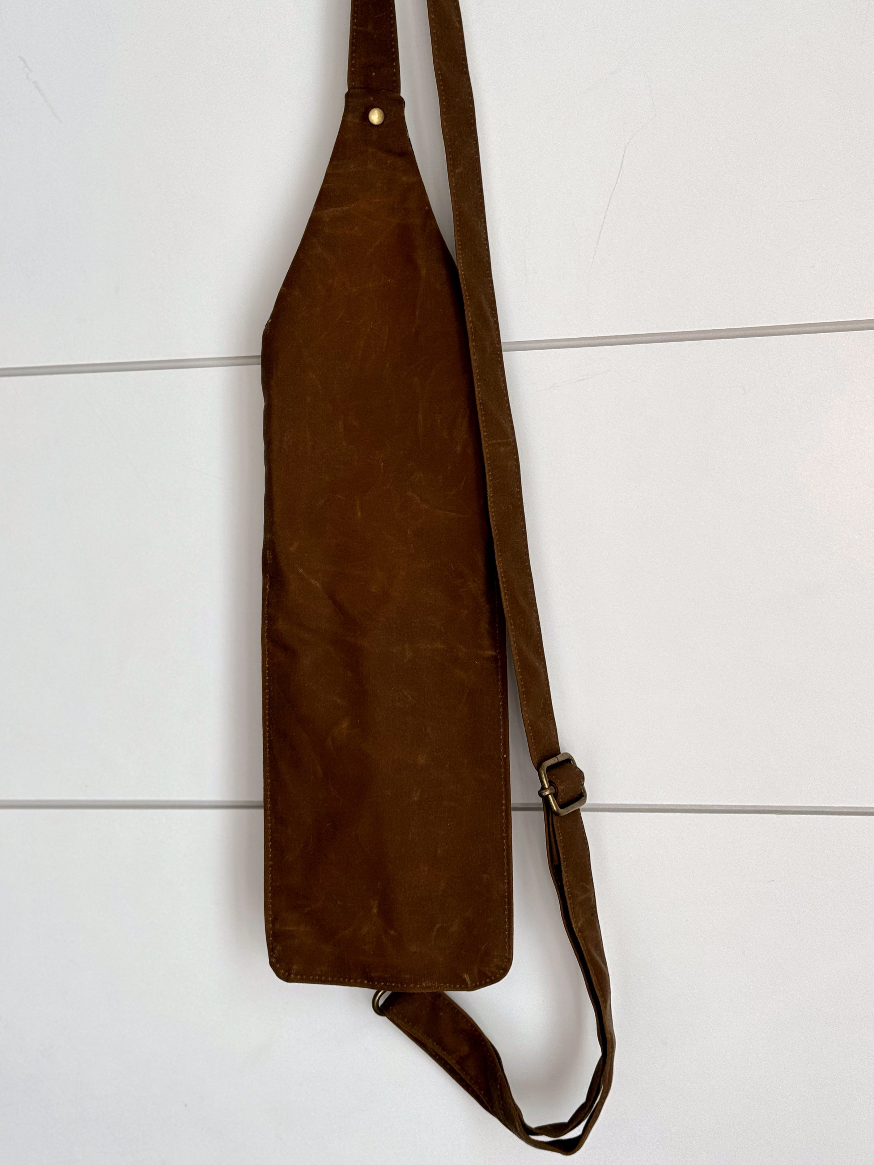 Back side of crossbody bag hanging with white background. In brown solid waxed canvas.