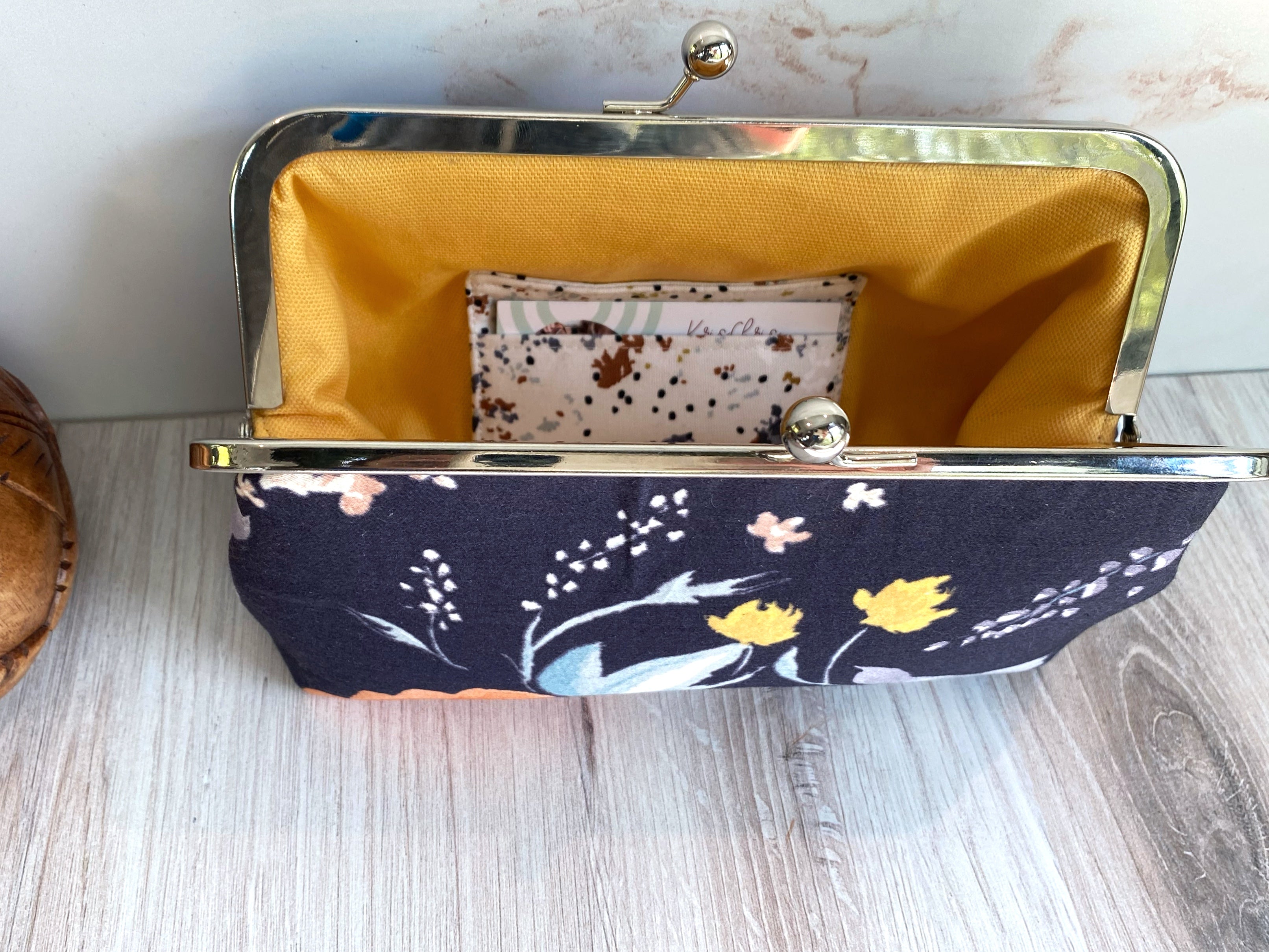 Opened kisslock clutch shows interior card pockets and yellow canvas lining as well as closeup of silver hardware.