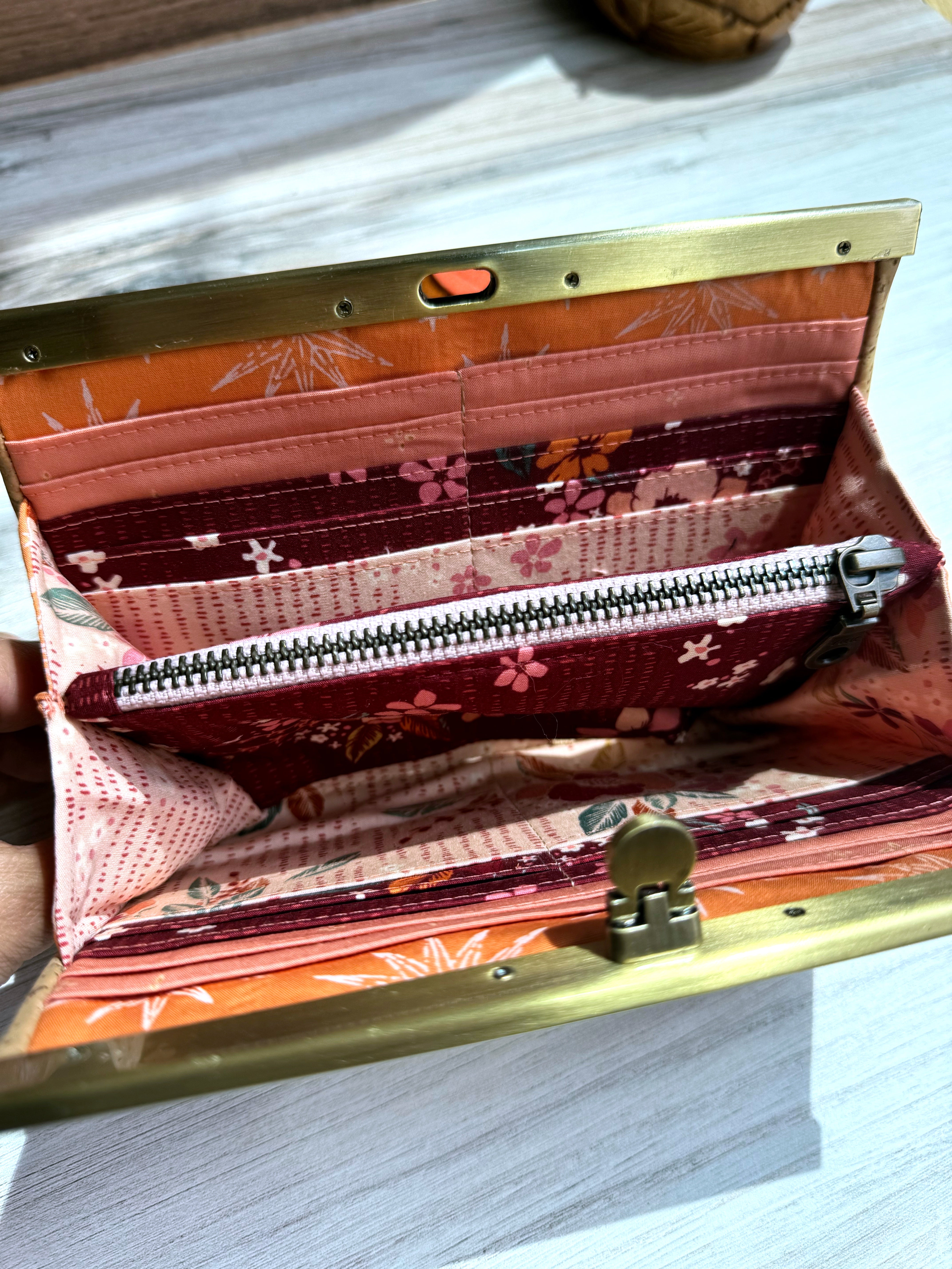 Open accordion wallet with pink, dark red, and orange interior fabrics with multiple card slots. Also interior pink zipper pocket.