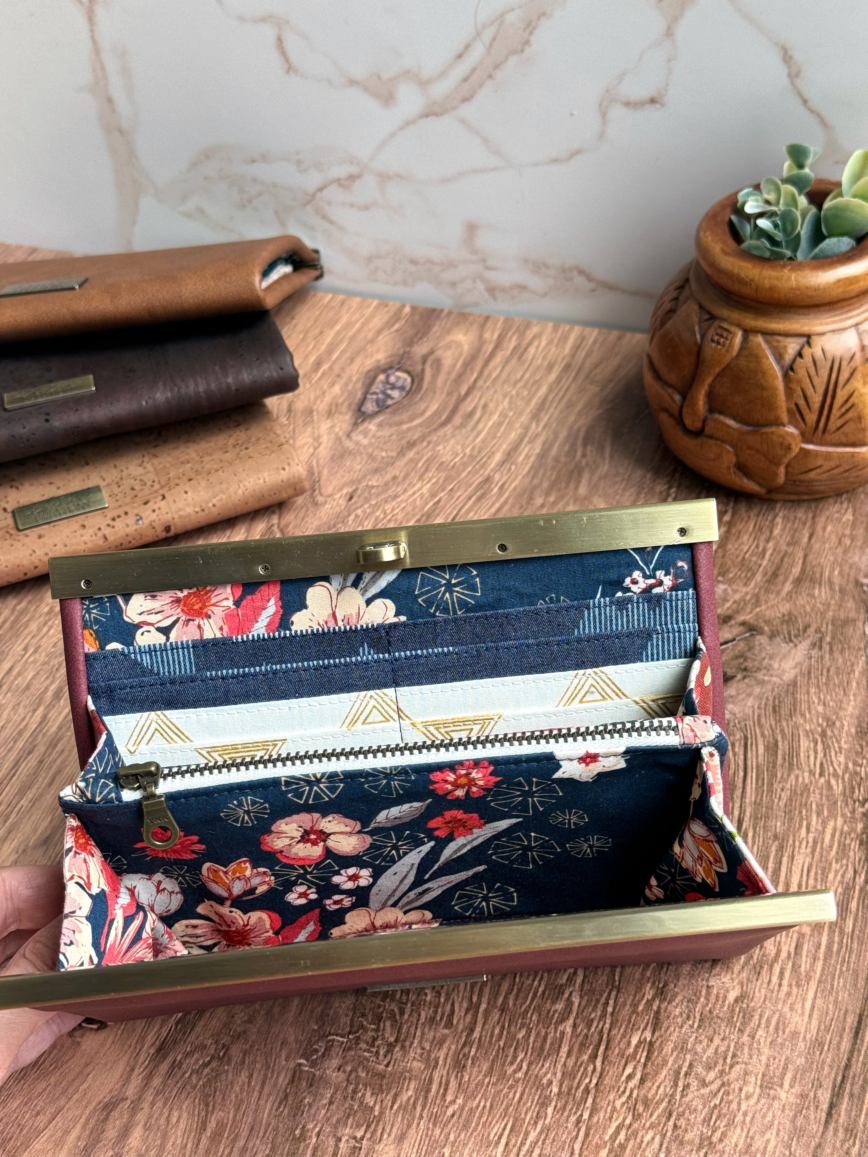Open accordion wallet with navy floral fabrics inside with 3 more wallets in background and wooden bowl with greens.