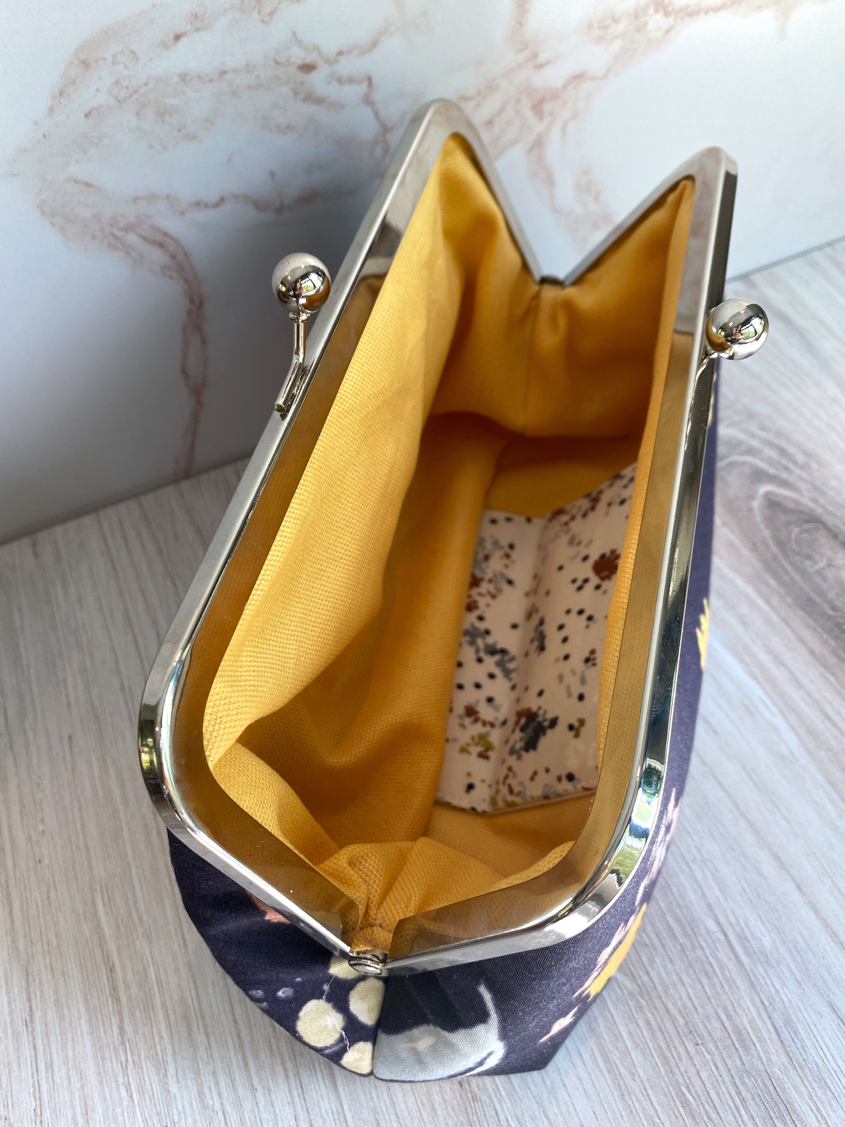 Opened twist lock clutch shows yellow canvas lining and interior card pockets.