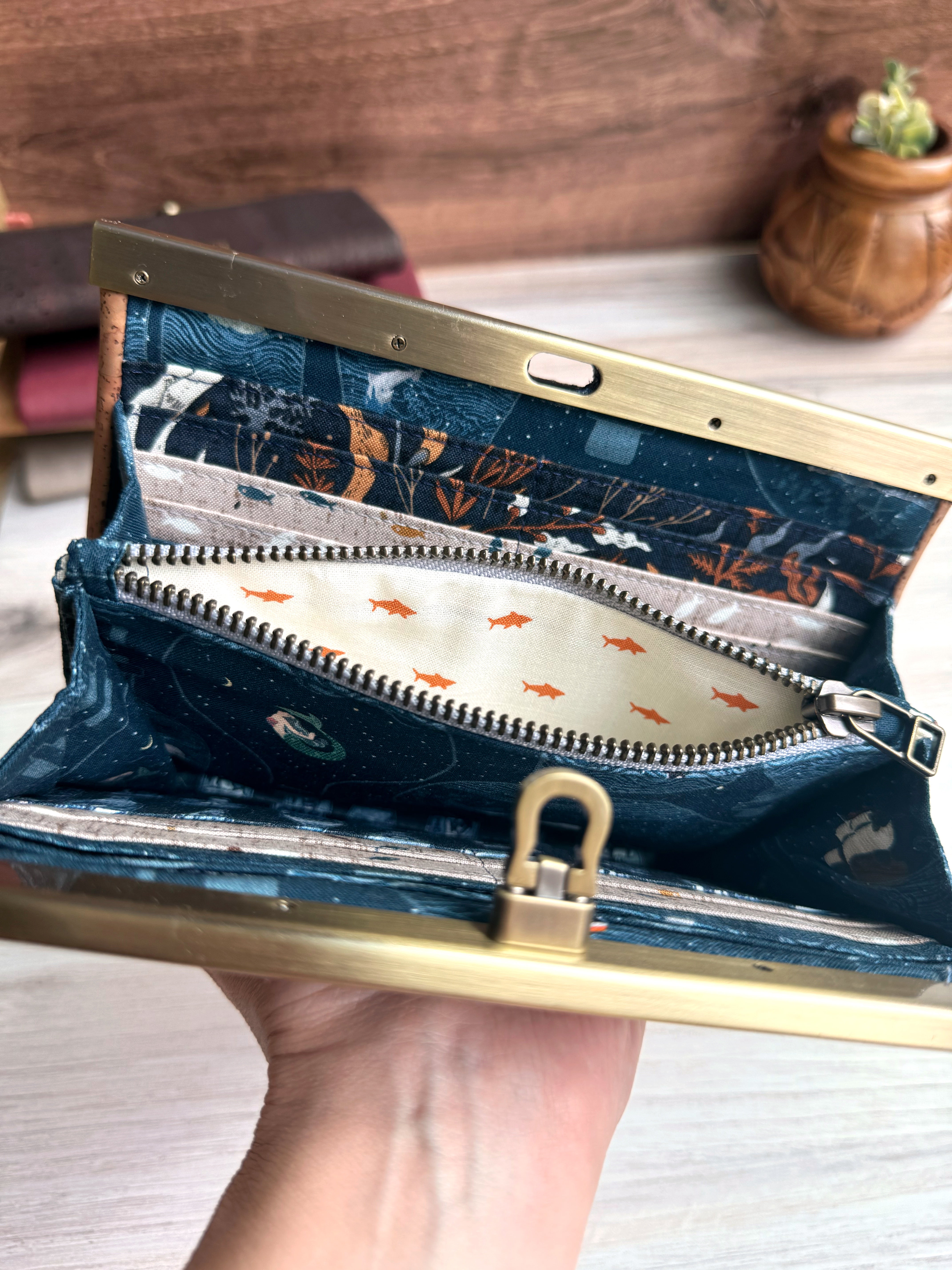 Open accordion wallet reveals interior ykk zipper opened to show orange sharks and a cream background. Remaining fabrics show mermaids, pirate bottles, fish, and underwater vines with plenty of card slots