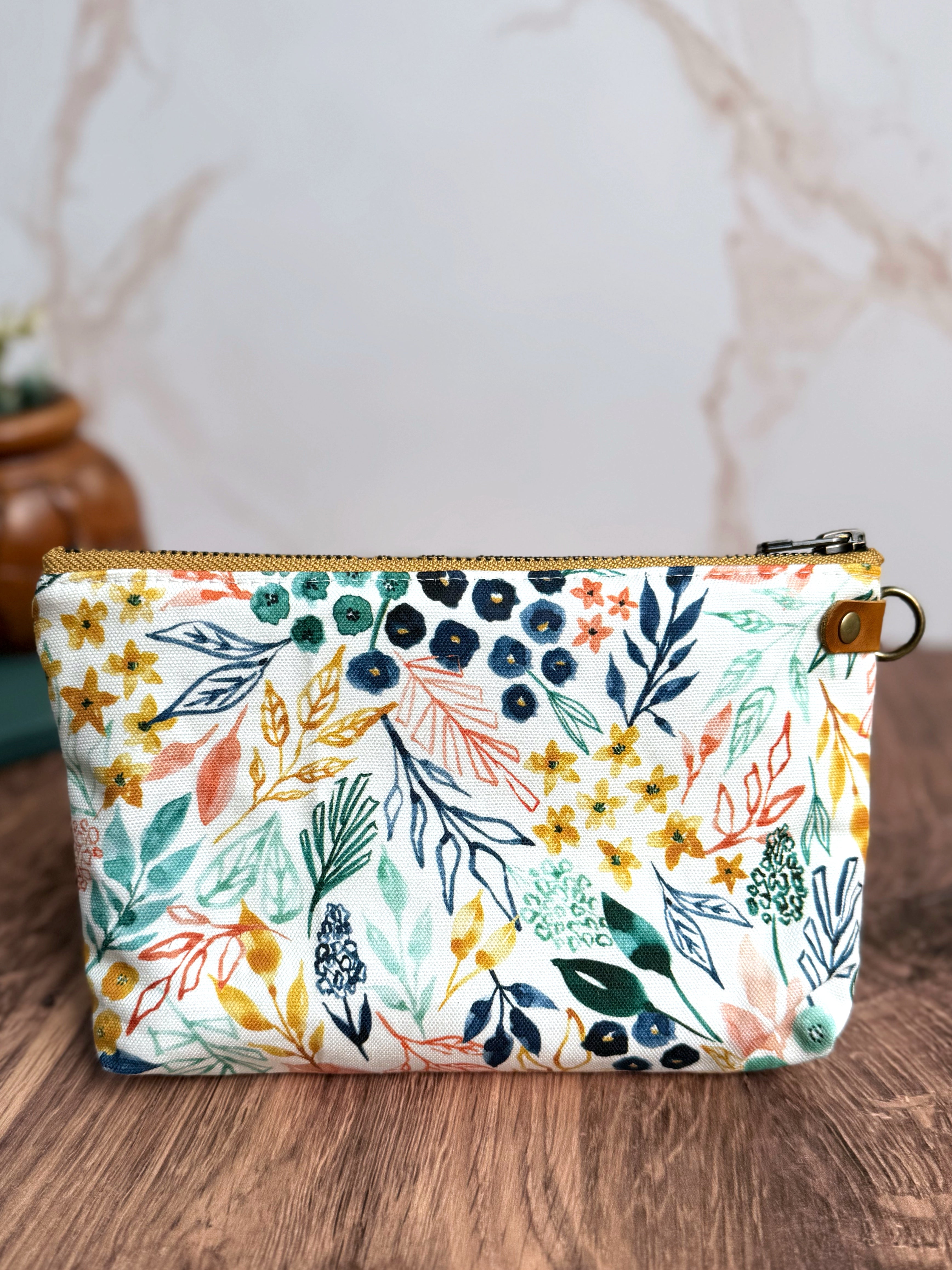 Pouch with bright white background and floral illustrated designs with navy, yellow, coral, and teal.