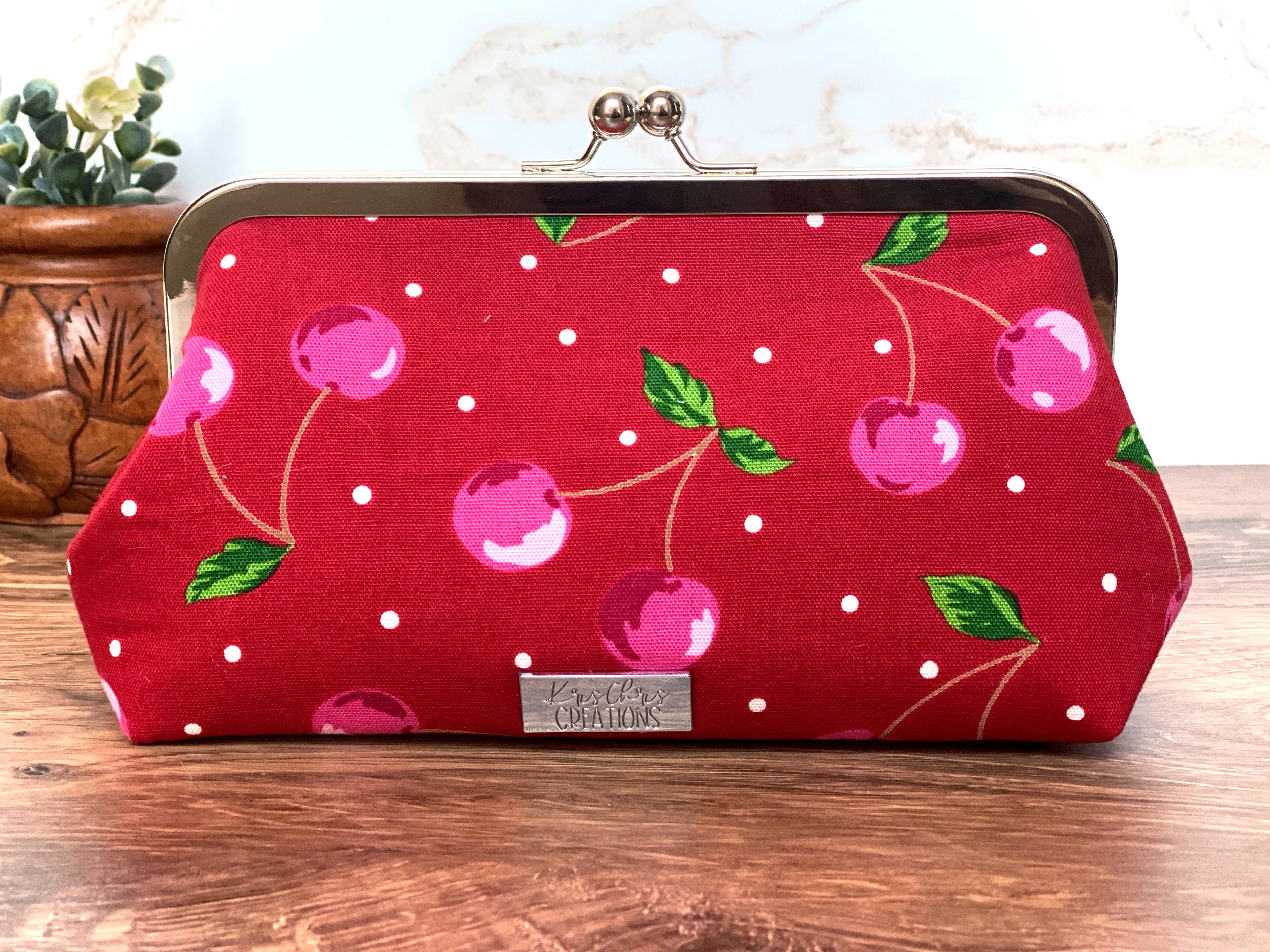 Twistlock cherry themed clutch bag with Silver hardware along top shows bright red canvas fabric and cheerful pink cherries all over.