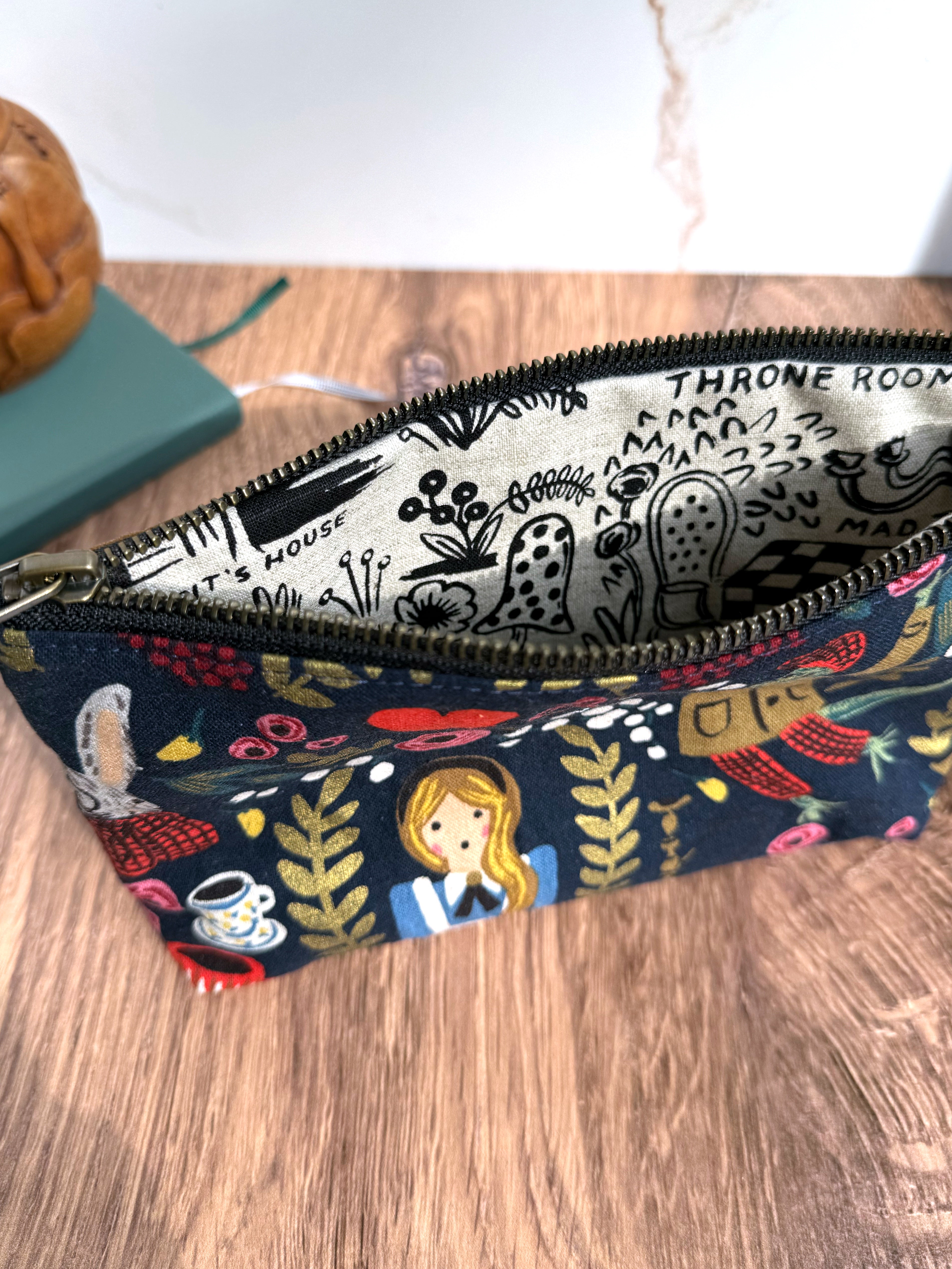 Open main zipper on Alice in Wonderland pouch shows black and white lining fabric - more Alice themed canvas illustrations.