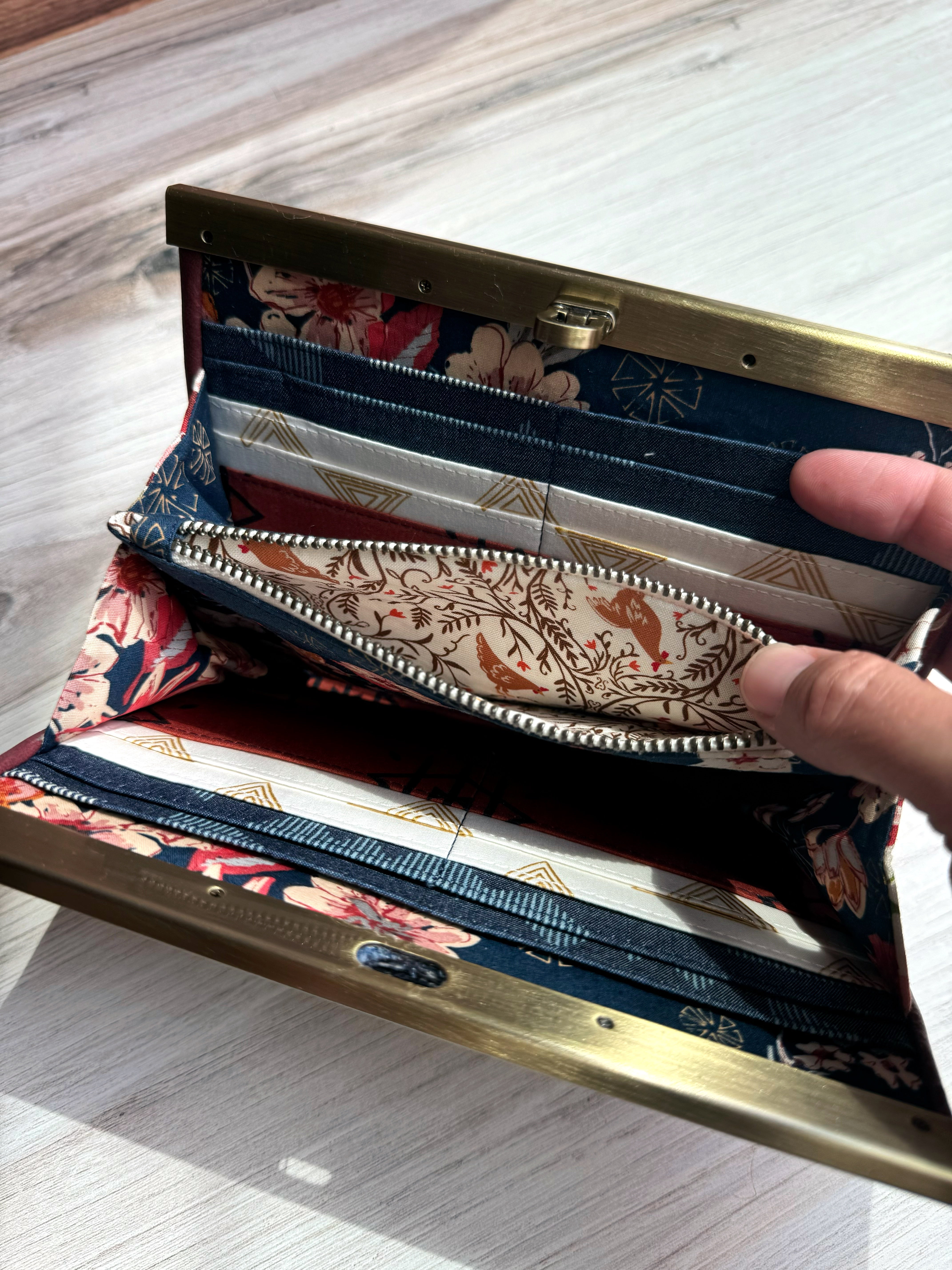 Open accordion wallet reveals an interior pocket with zipper closure that has sweet rooster fabric and ornate floral designs.