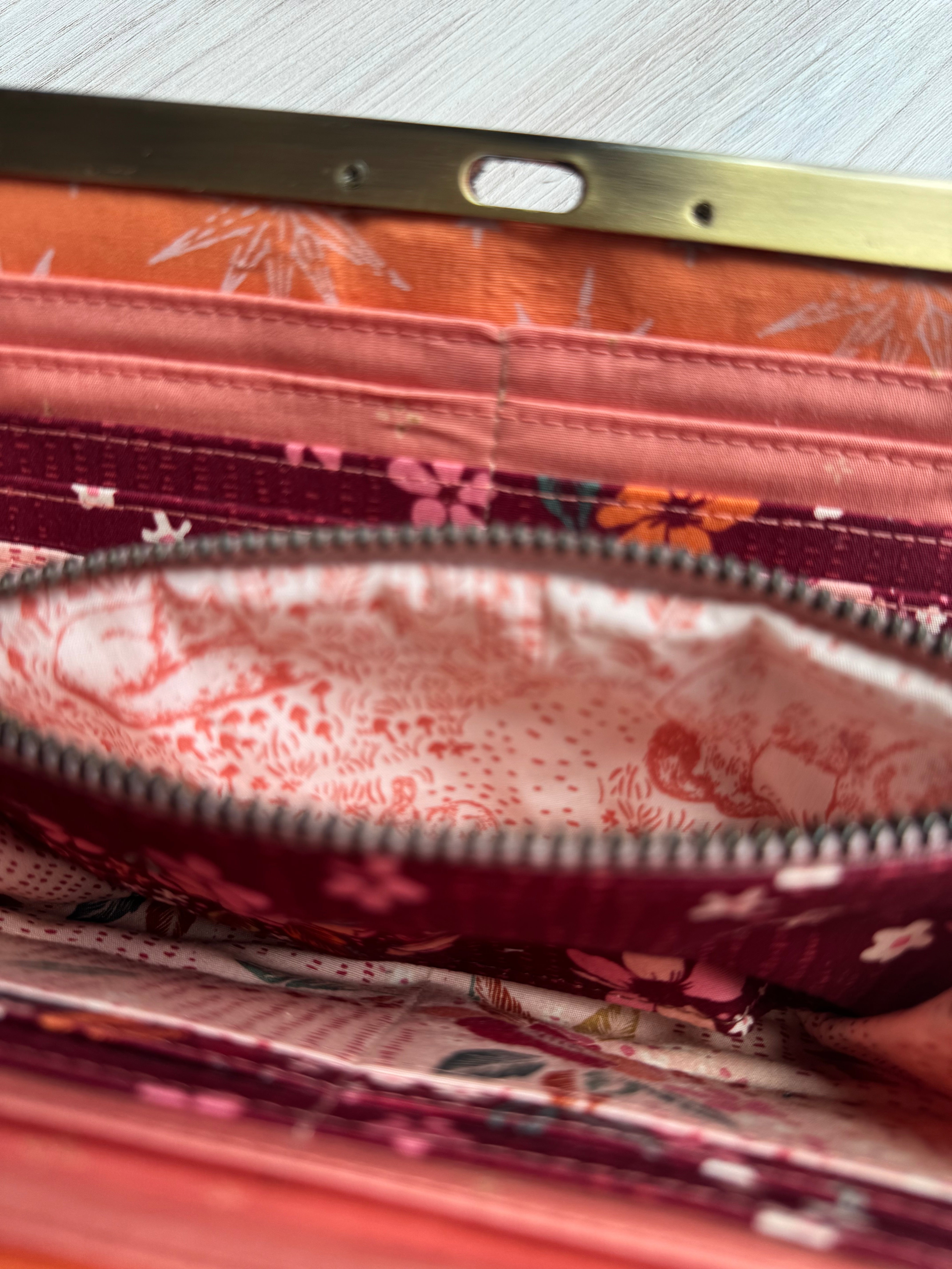 Open accordion wallet with pink, dark red, and orange interior fabrics with multiple card slots. Interior open zipper shows woodland animal fabric.