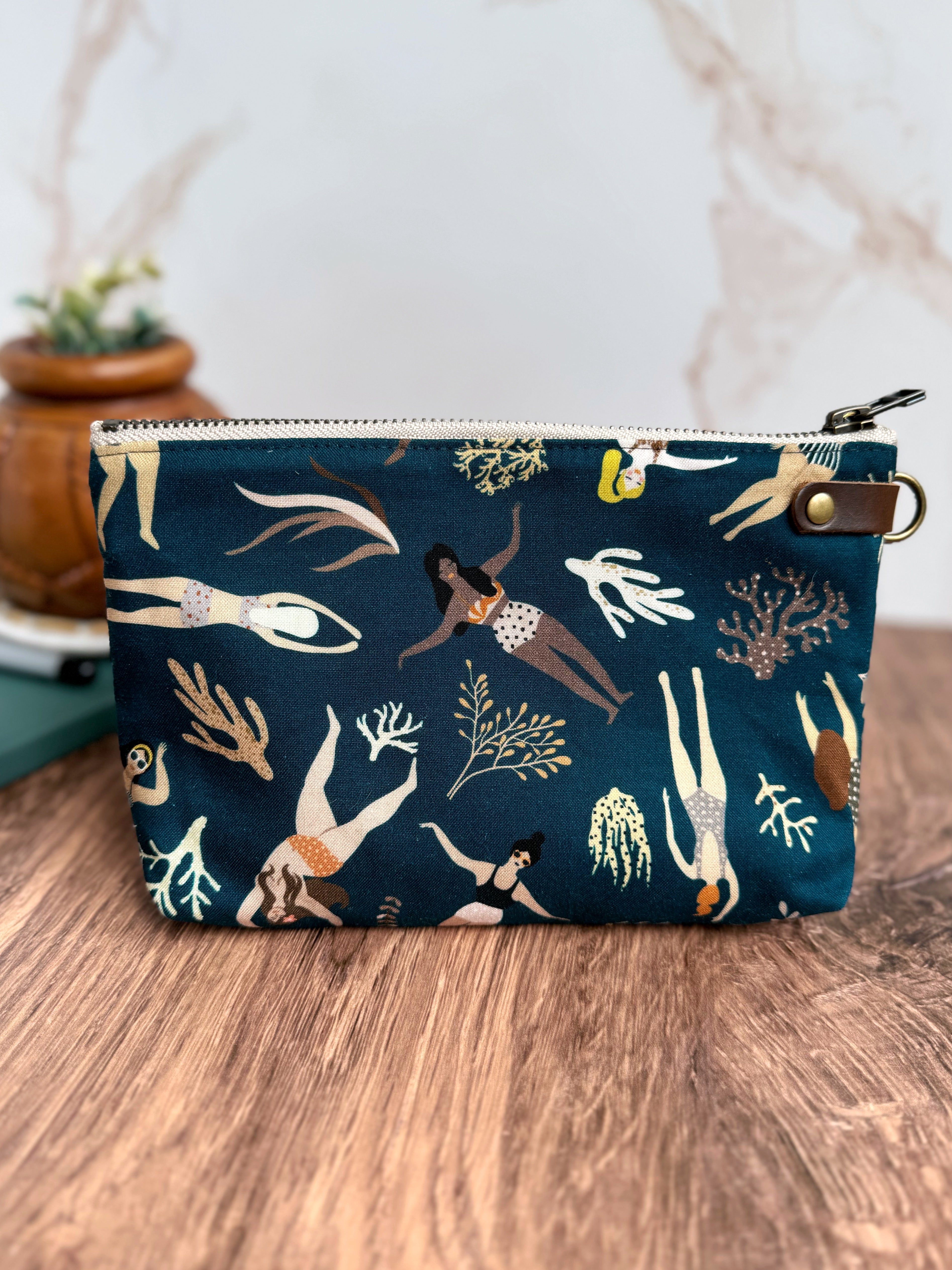 Back view of pouch with dark teal fabric featuring ladies in bathing suits swimming