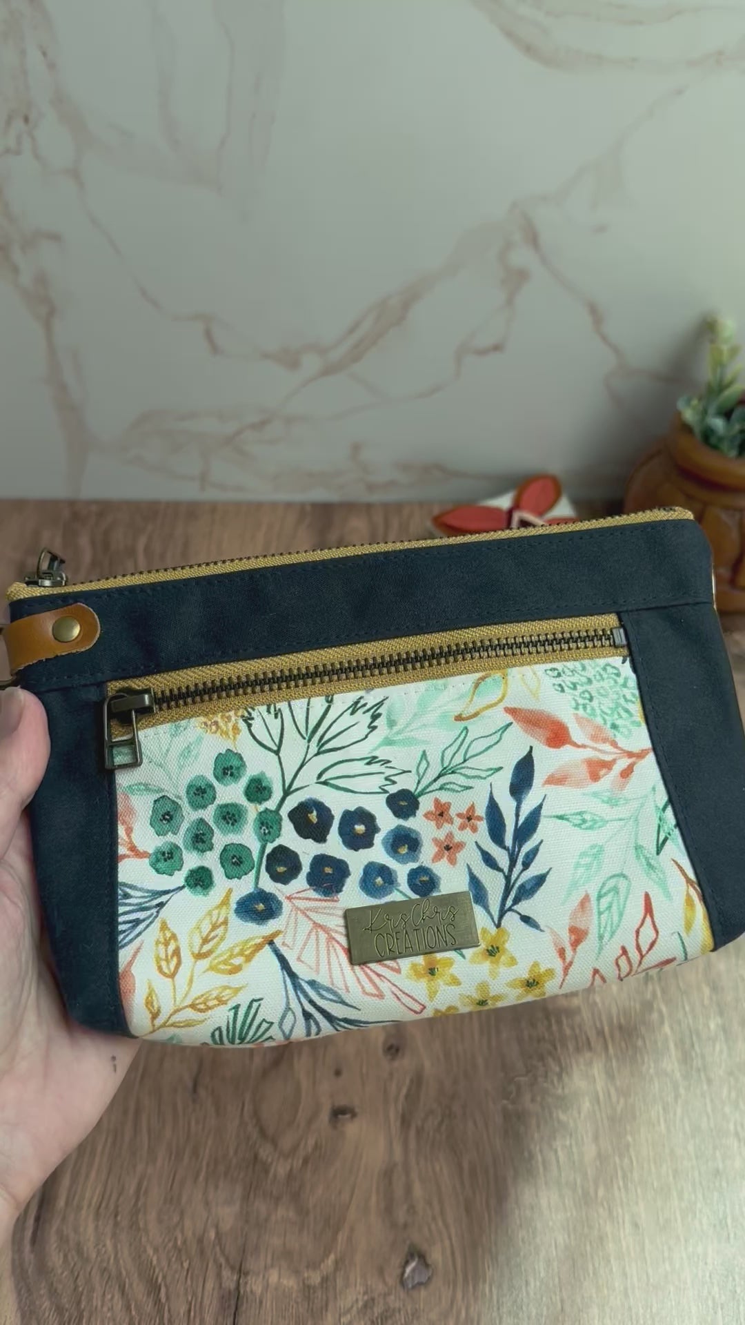 Floral pouch with yellow zippers in hand shown on both sides and with zippers opening to reveal coordinating navy and teal lining fabrics.