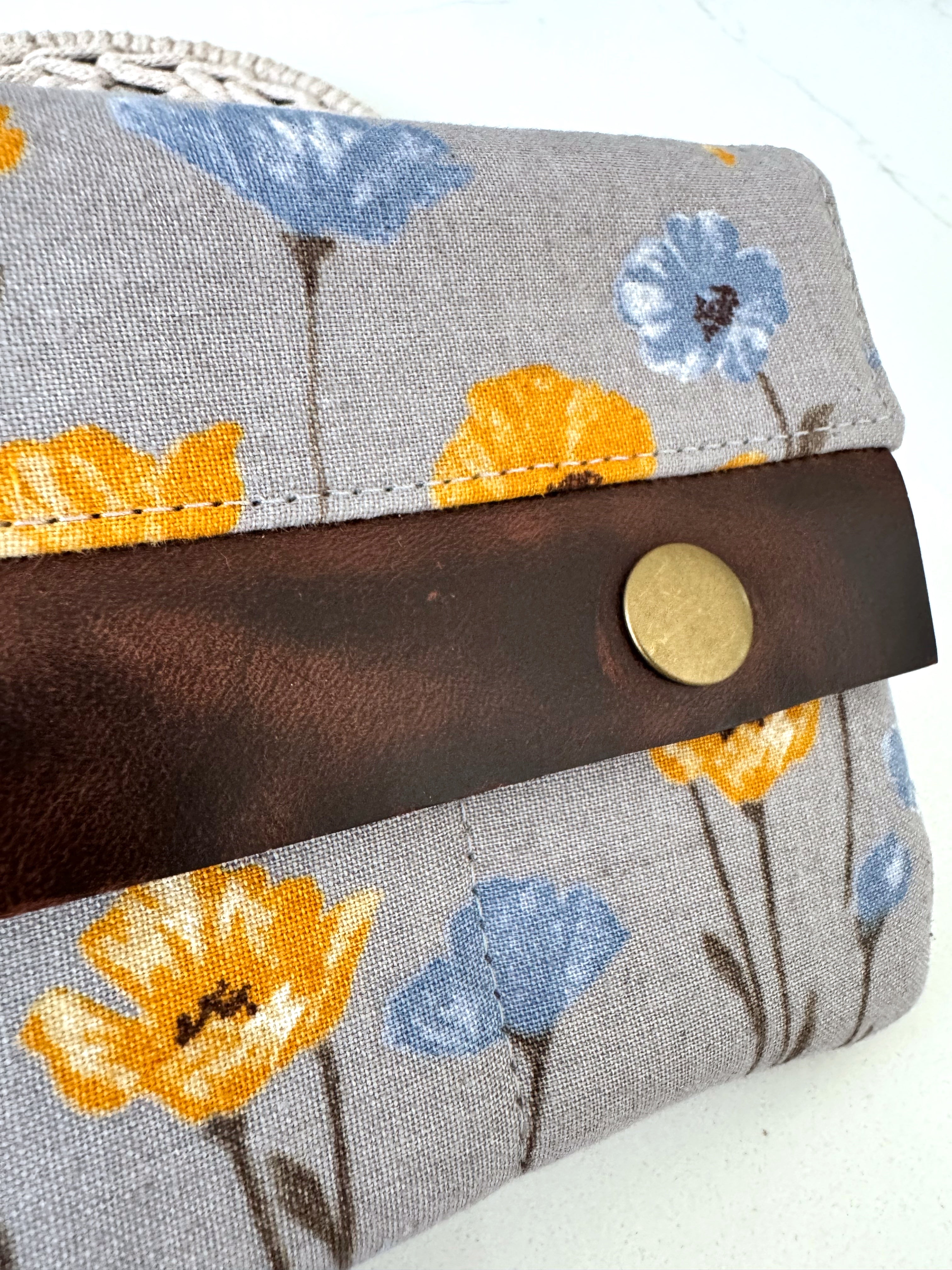 Floral-patterned fabric pouch with leather strap and button on a white background