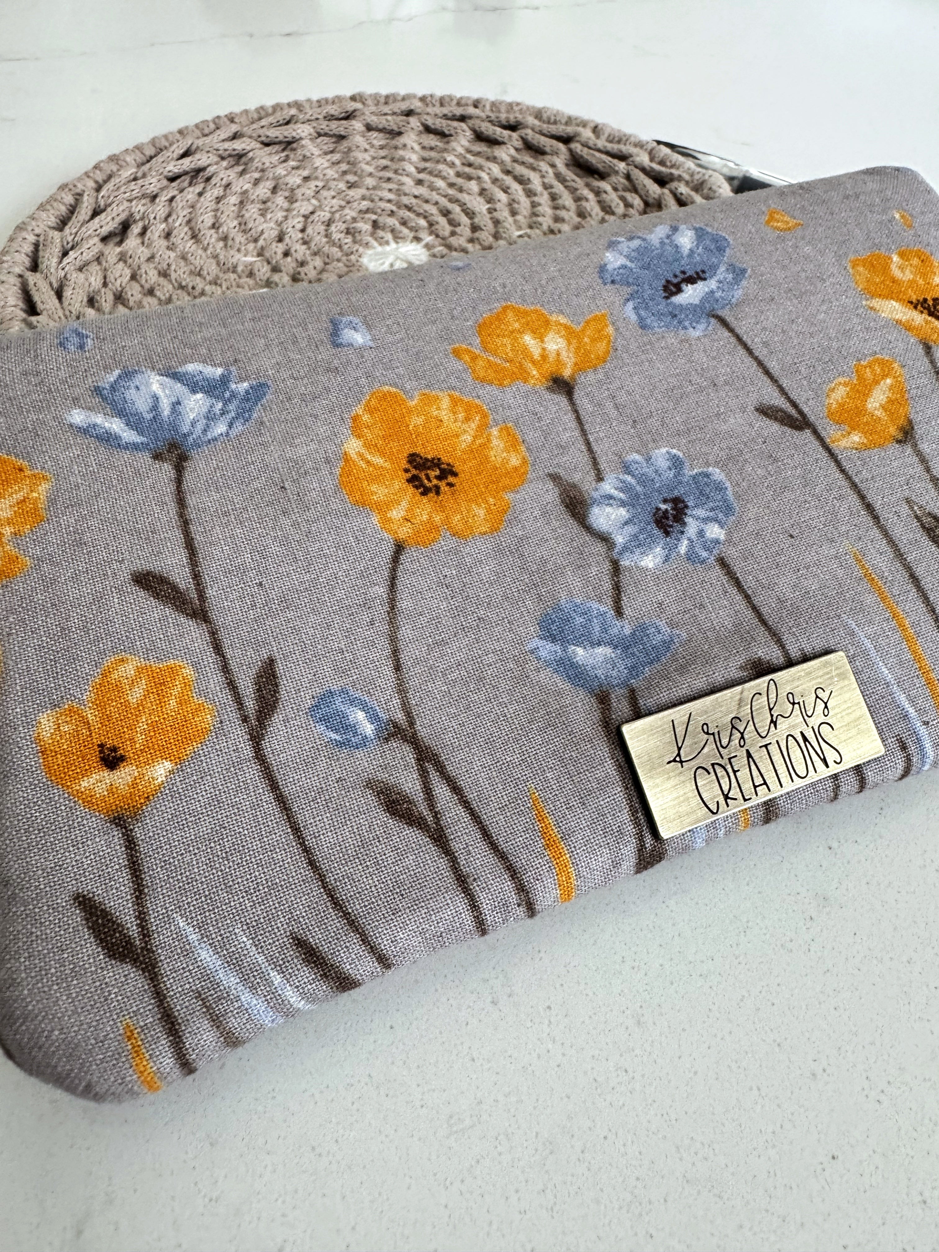 Closeup of a gray wallet with yellow and blue flowersand brass label. 