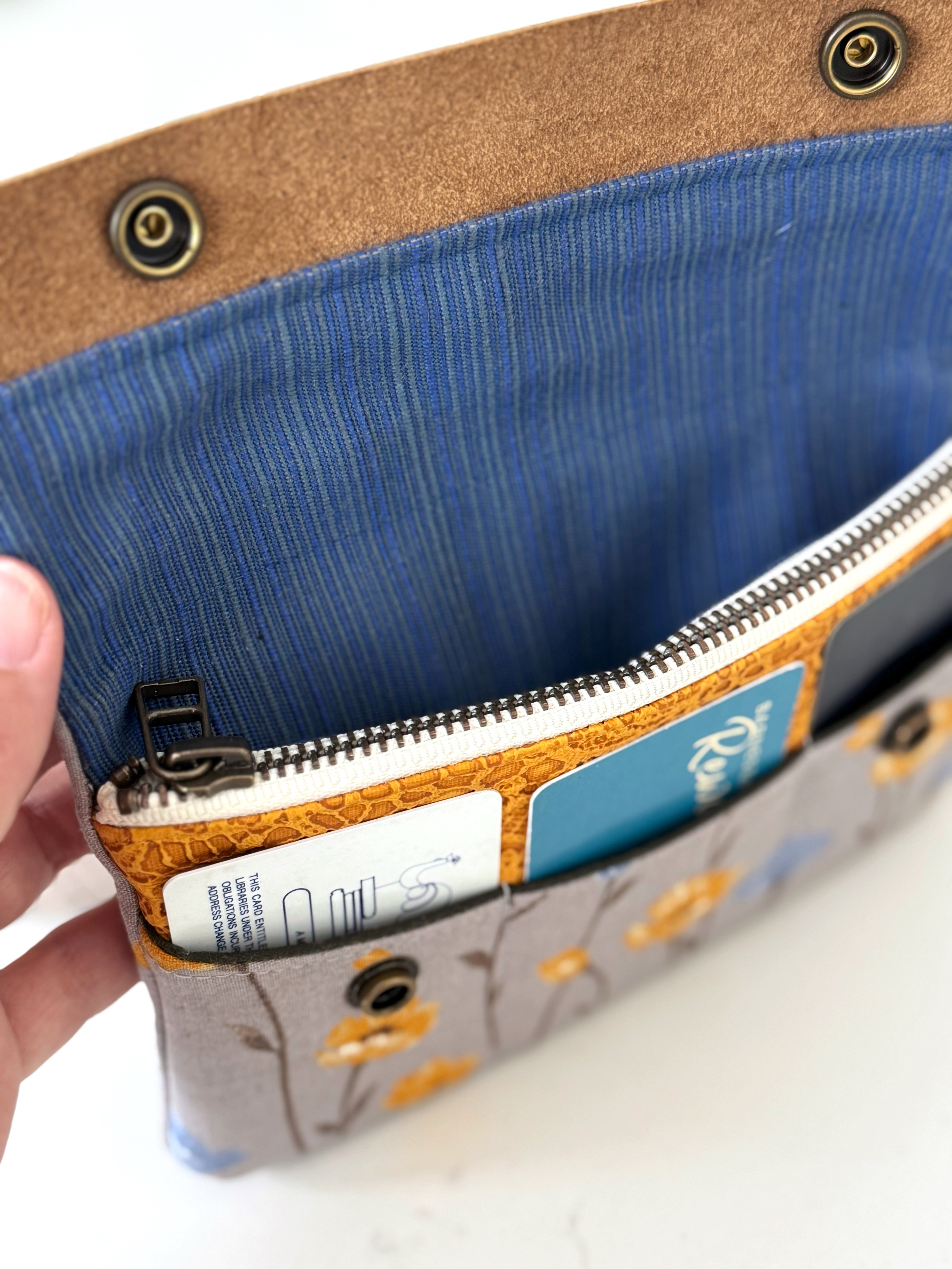 Close-up of a blue pouch with a zipper, held by a hand on a white background.