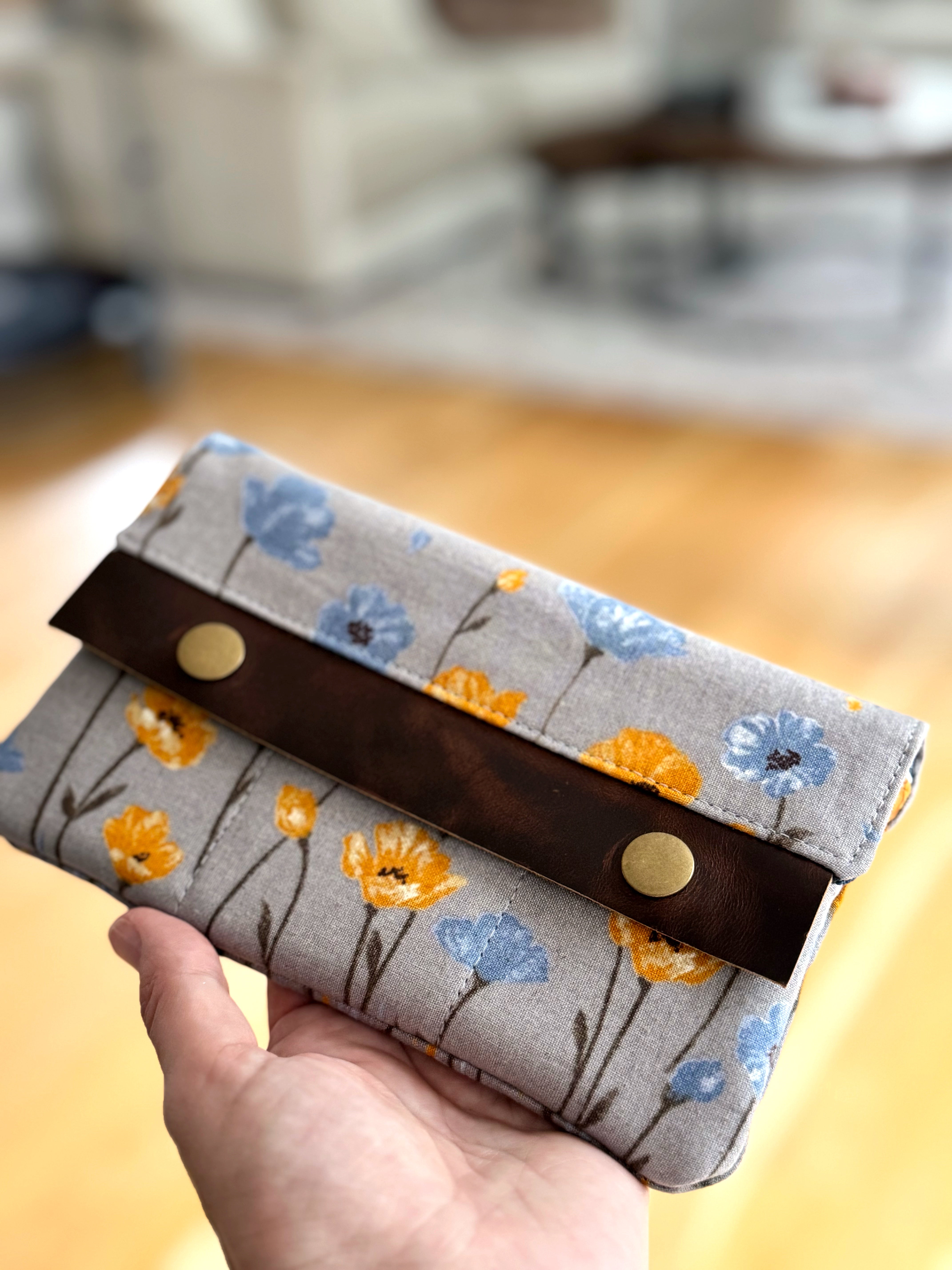 Hand holding a fabric pouch with floral pattern and brown leather tab.