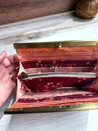 Open accordion wallet with pink, dark red, and orange interior fabrics with multiple card and cash slots.