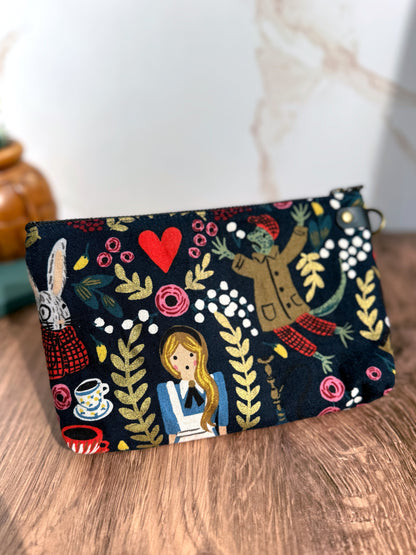 Back of Erin pouch shows Rifle Paper Co. Alice in Wonderland abirc with Alice, rabbit, frog, heart, tea cups and floral designs.