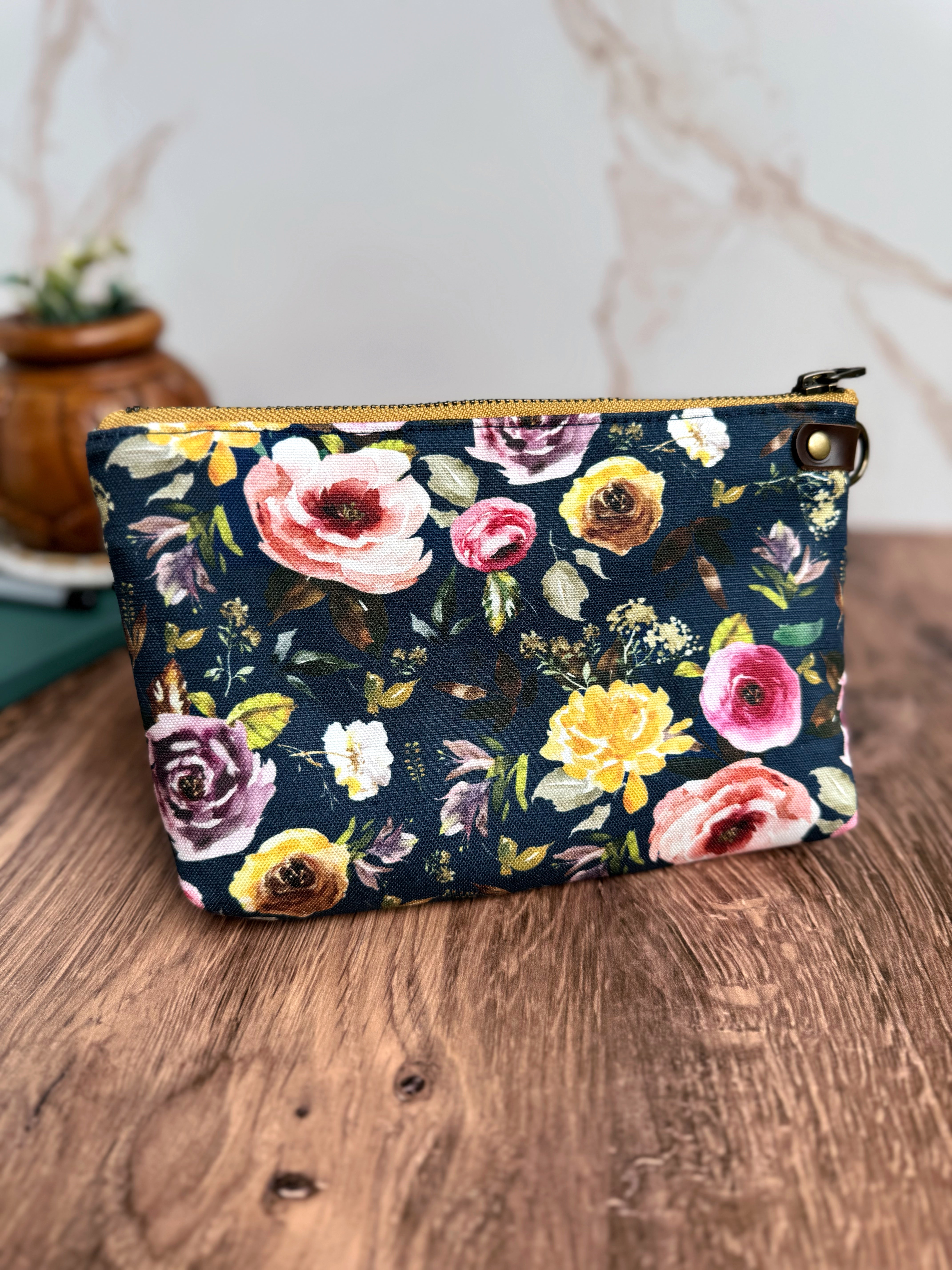 Bright floral fabric pouch. Fabric has navy background and yellow, pink, and purple roses.