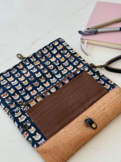 Clutch bag is opened flat on table to show full size with interior zippered pocket, 8 card slots in brown waxed canvas. Tan cork base is at the bottom.