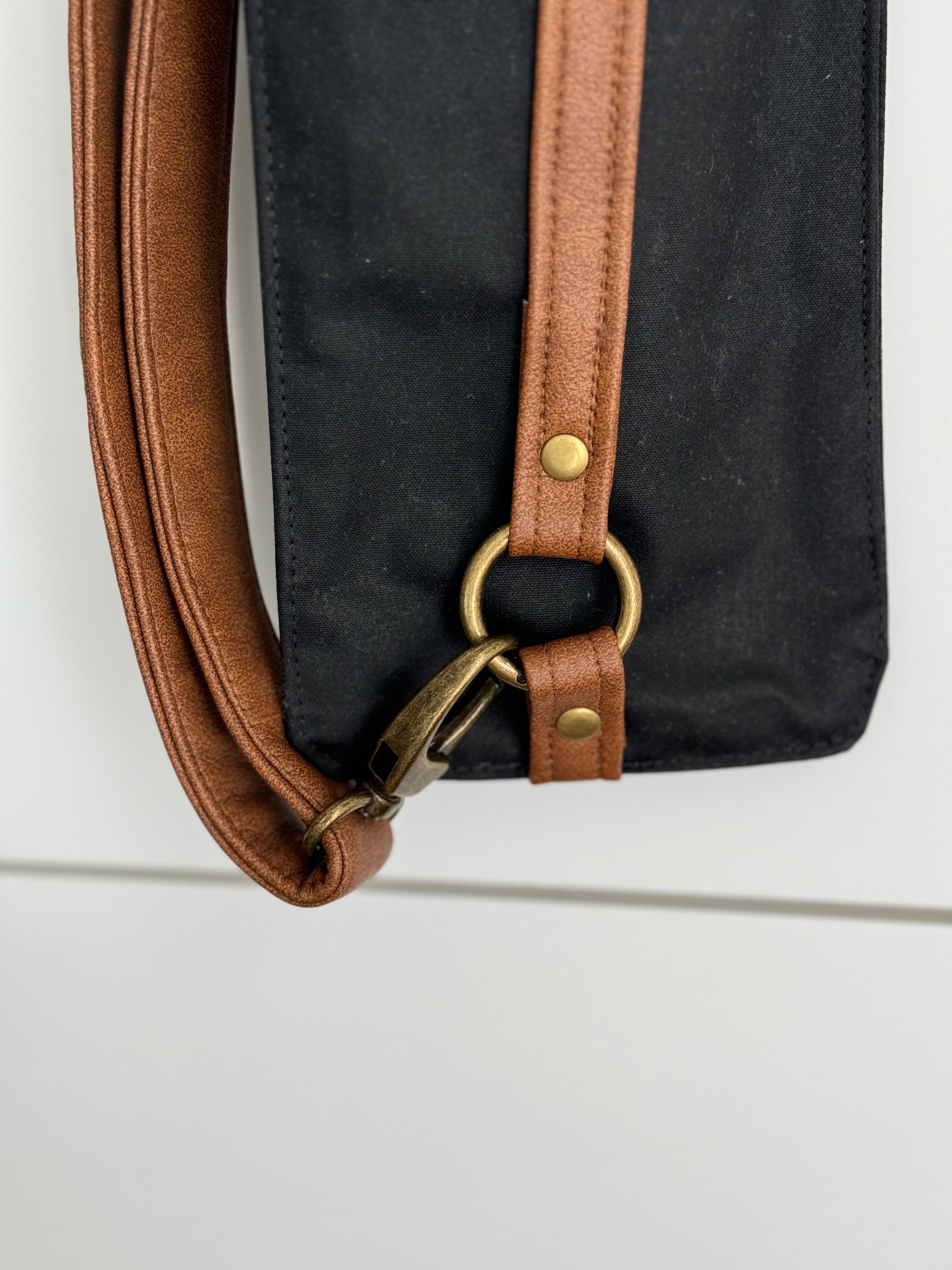 Close up view of tan vegan leather straps and lobster clasp holding adjustable strap in place as well as gold rivets.