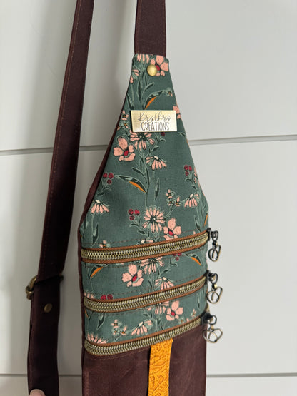 Crossbody bag hanging in the light showing lovely teal floral fabrics and brass zippers across.