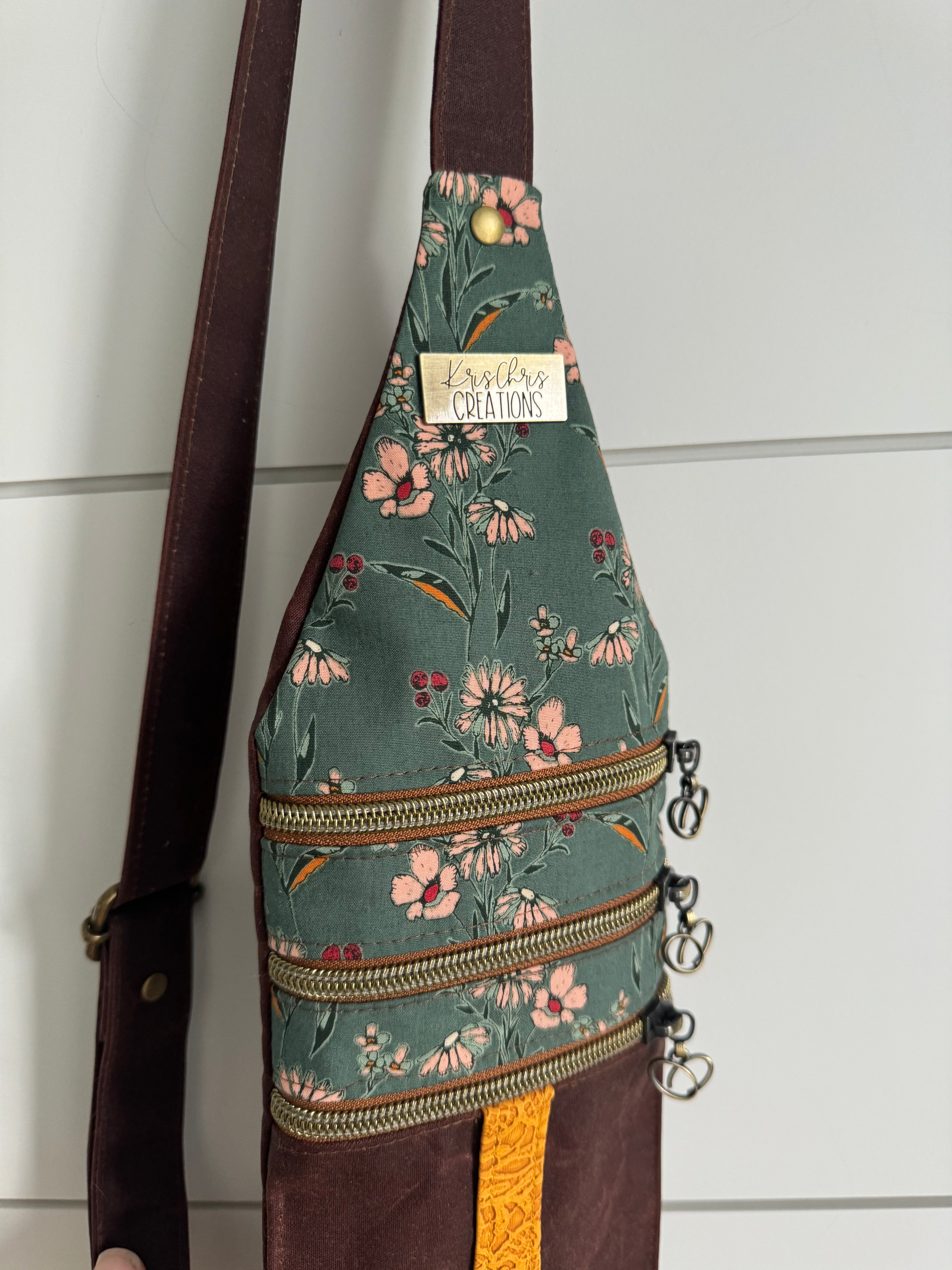 Crossbody bag hanging in the light showing lovely teal floral fabrics and brass zippers across.