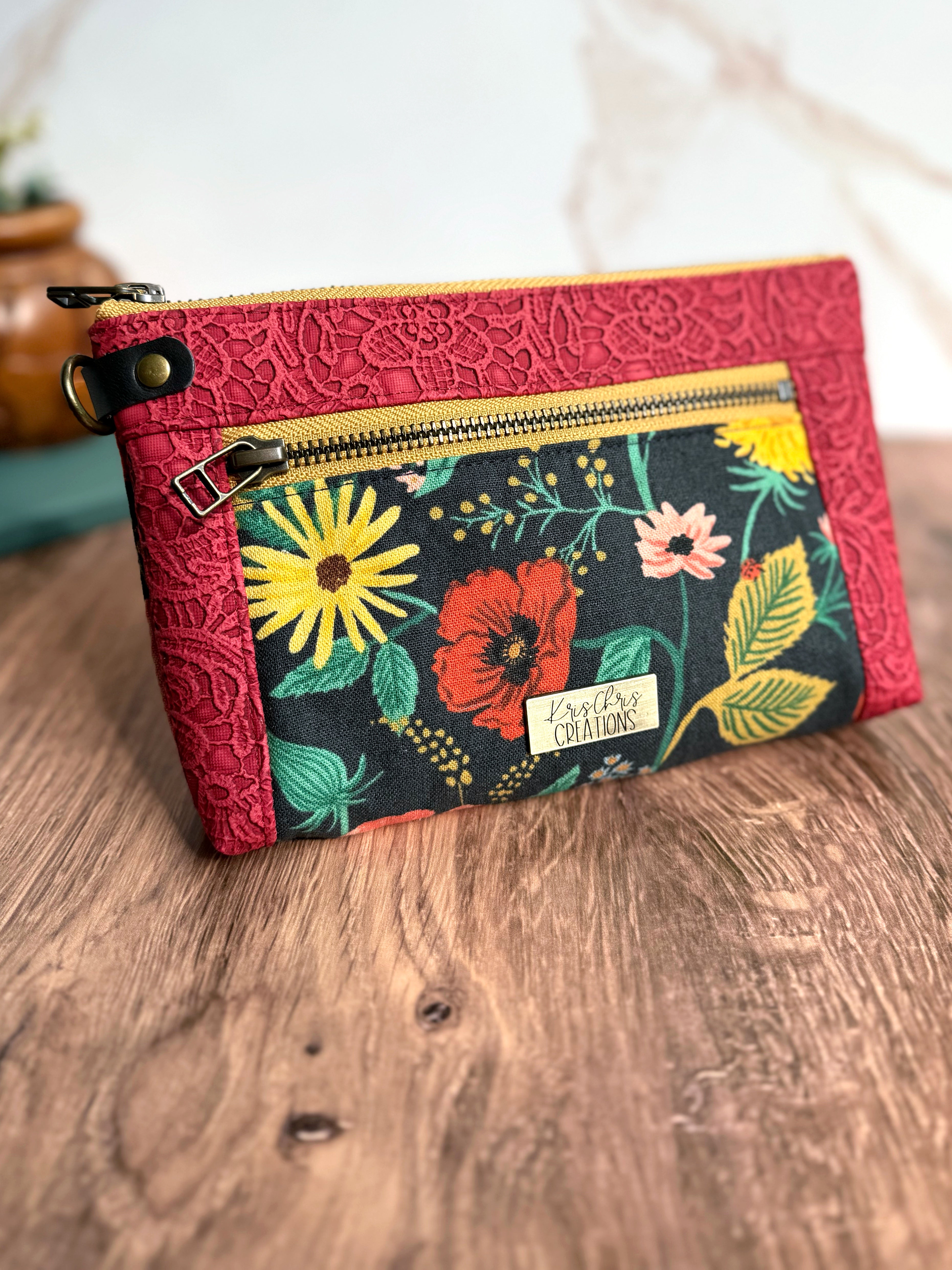 Floral pouch in Rifle Paper Co fabric and red lace vinyl trim. There are yellow fabric zipper, antique brass hardware, and leather side tab.