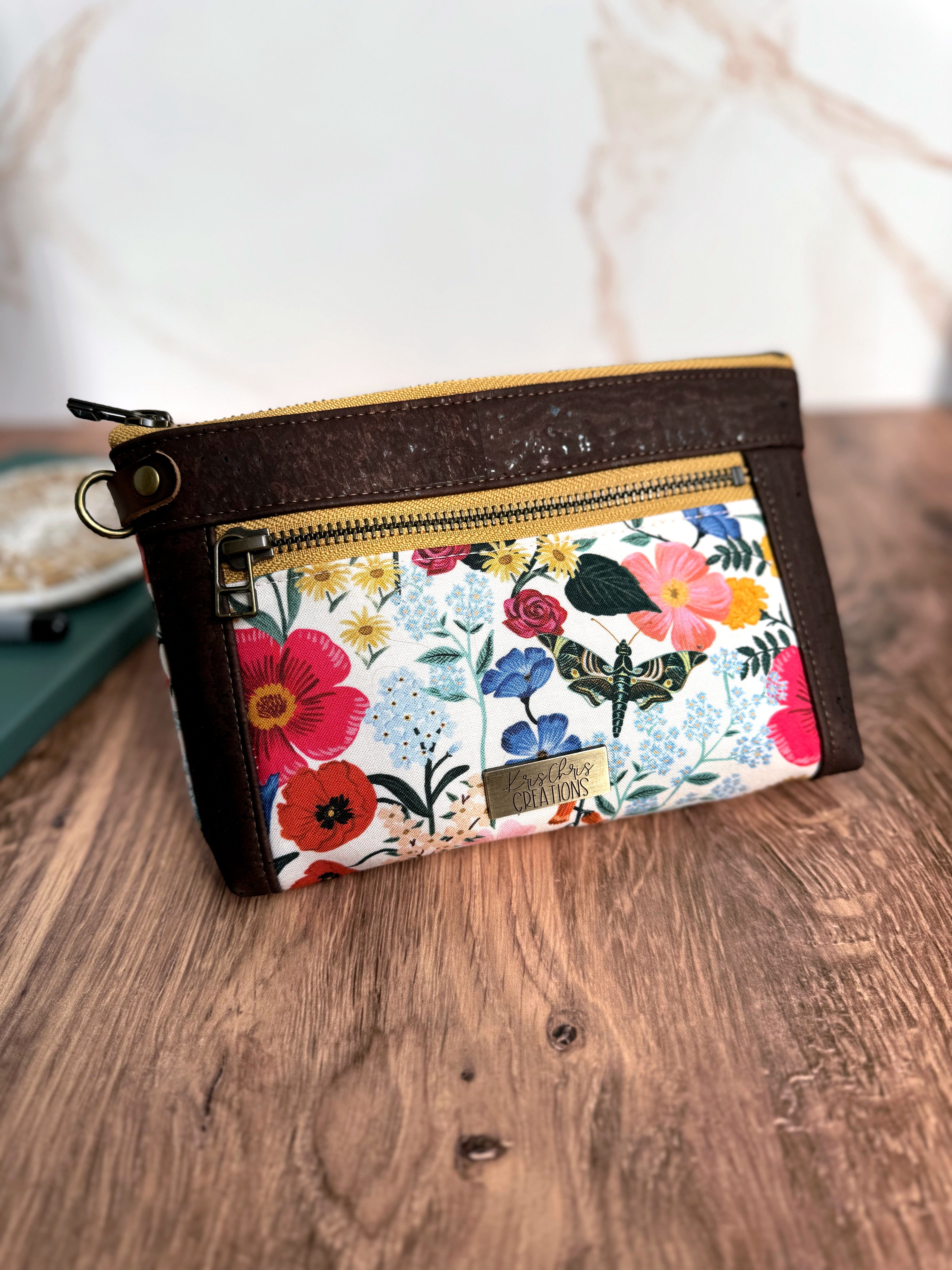Floral pouch with butterflies and bright colors and 2 yellow zippers in antique brass with chocolate brown cork trim and a leather tab and d ring on side. 