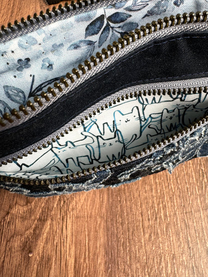 2 zippers on blue pouch are open to show cute illustrated cats in smaller pocket and blue floral designs on bigger pouch pocket.