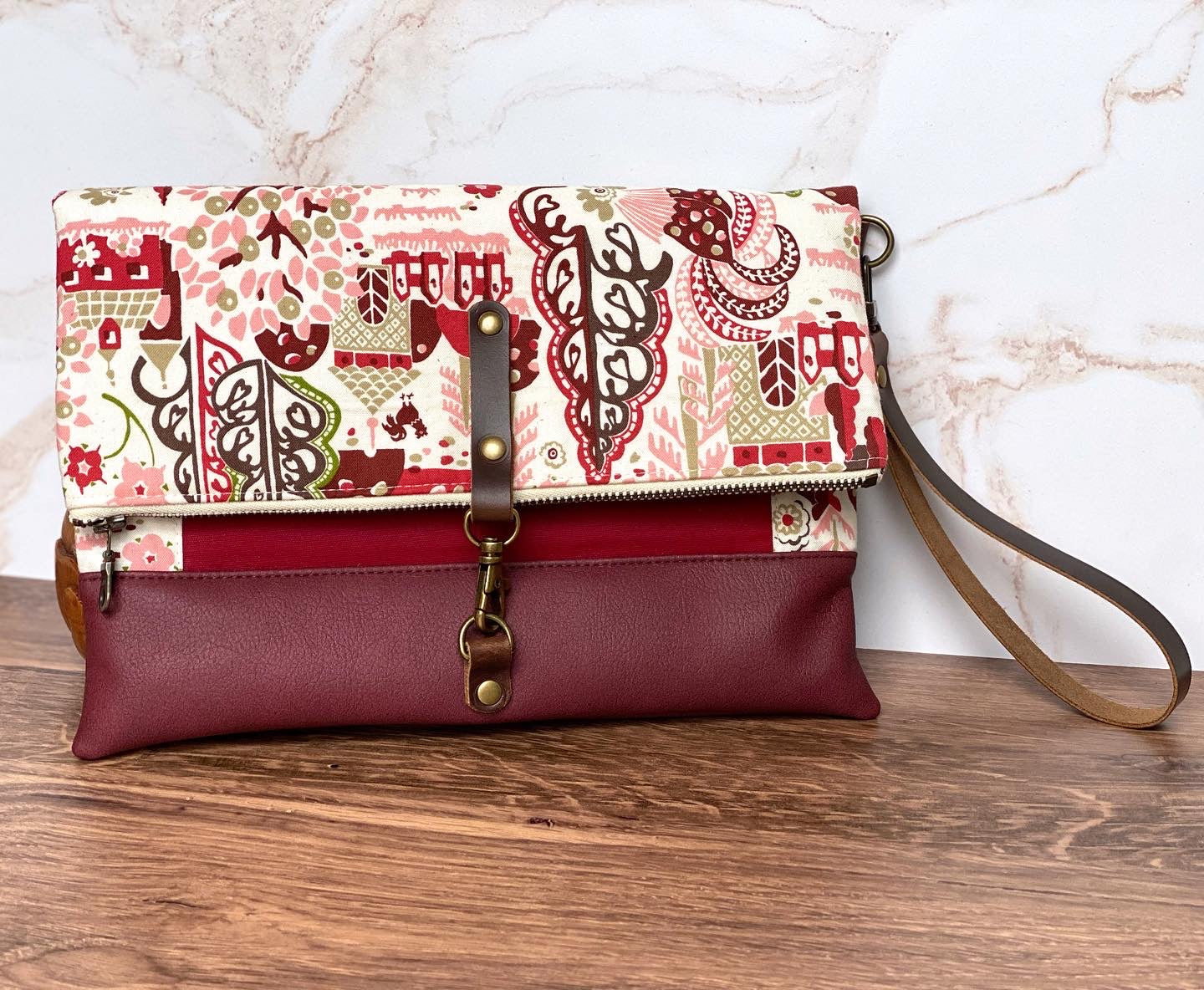 cream and maroon foldover clutch  with leather tab clasp and leather wrist strap. little houses and and floral fabric details