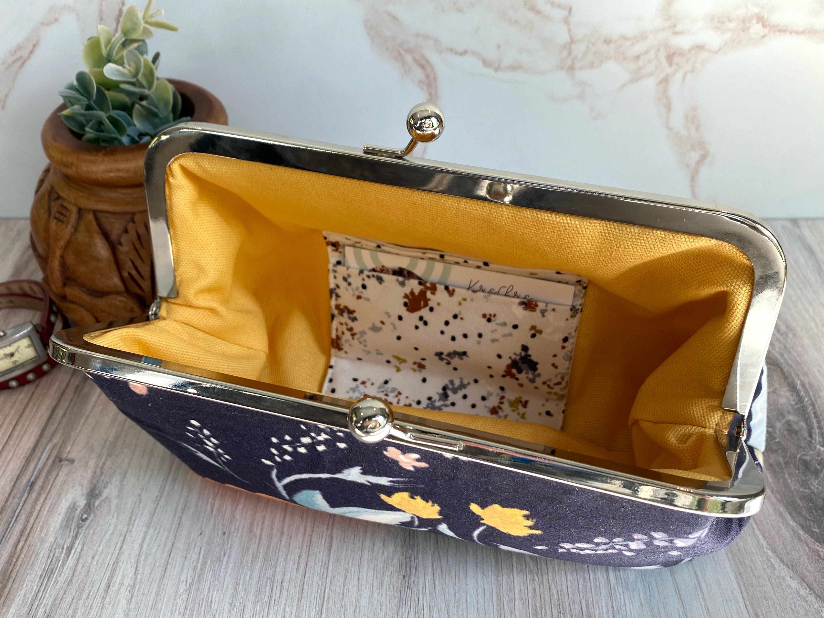 Floral navy clutch opened to reveal interior card slots and yellow canvas interior