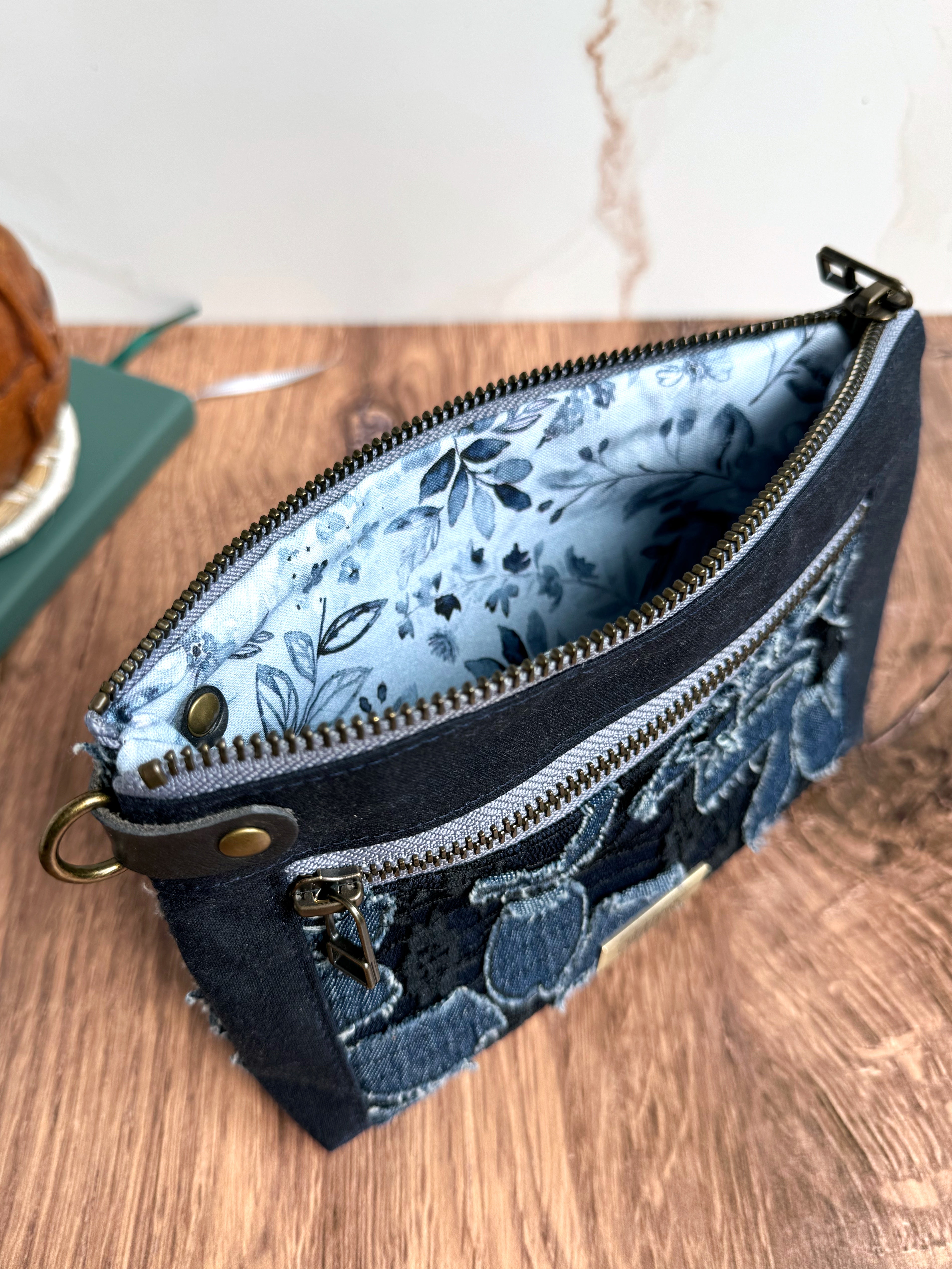 Open floral navy pouch on wooden base.  Antique brass rivets keep D ring tab in place.