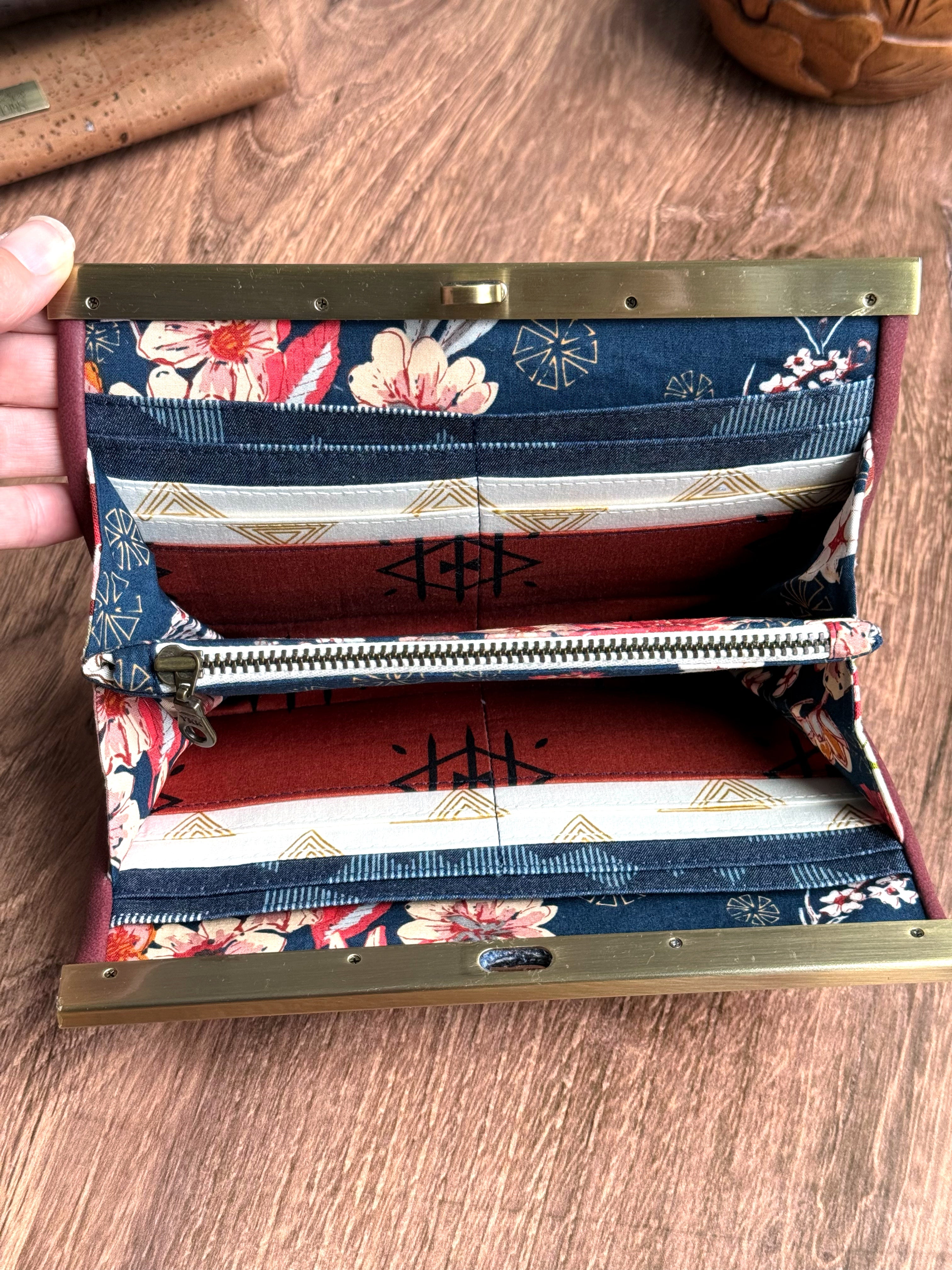 Open accordion wallet shows navy blue floral fabrics and geometric patterns on zippered interior pocket and many card slots.