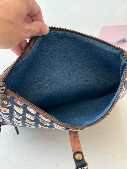 Top zipper on cat clutch is opened to show denim interior of main bag compartment which expands the full length of the clutch. 
