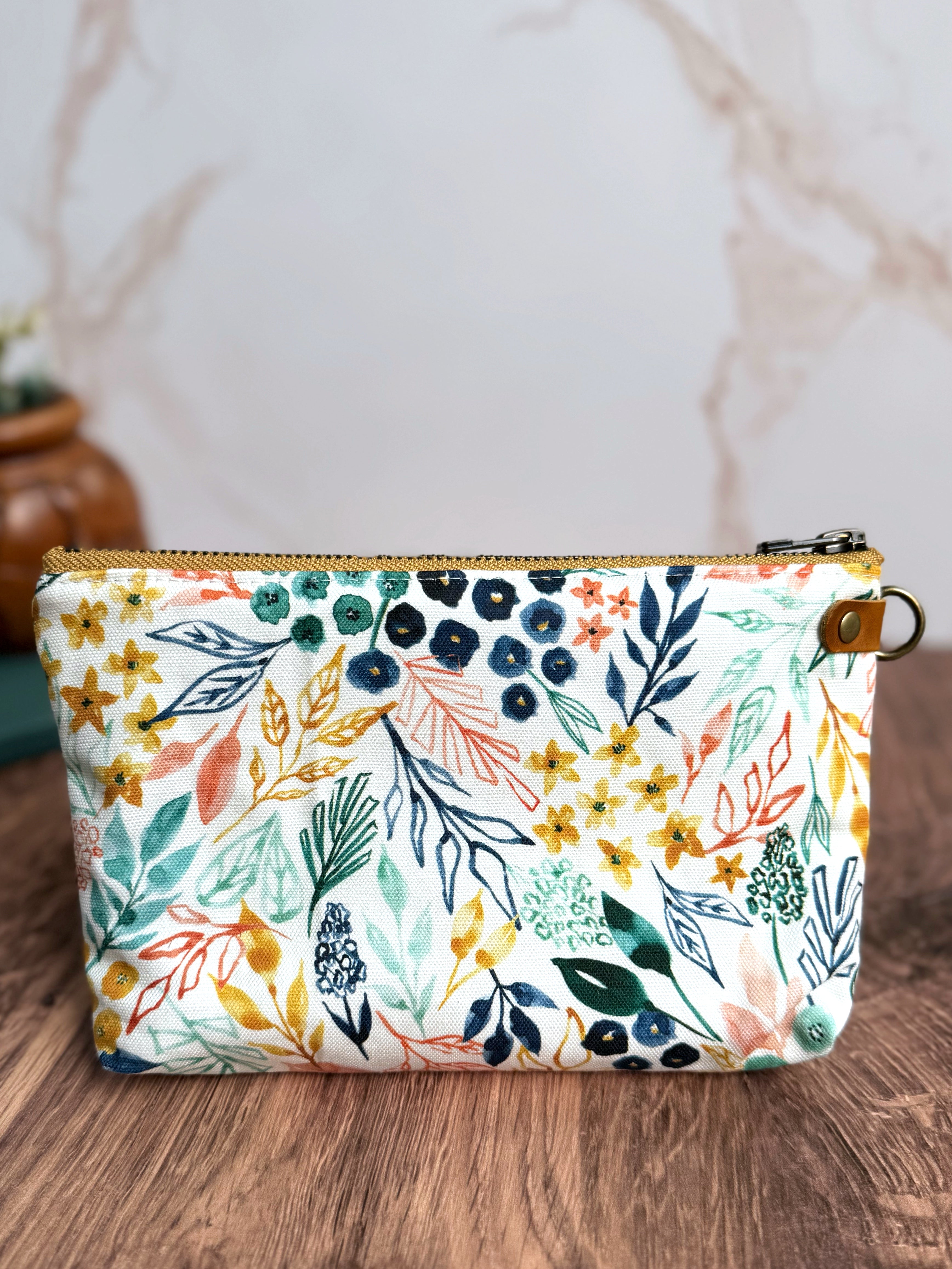 Pouch with bright white background and floral illustrated designs with navy, yellow, coral, and teal. 