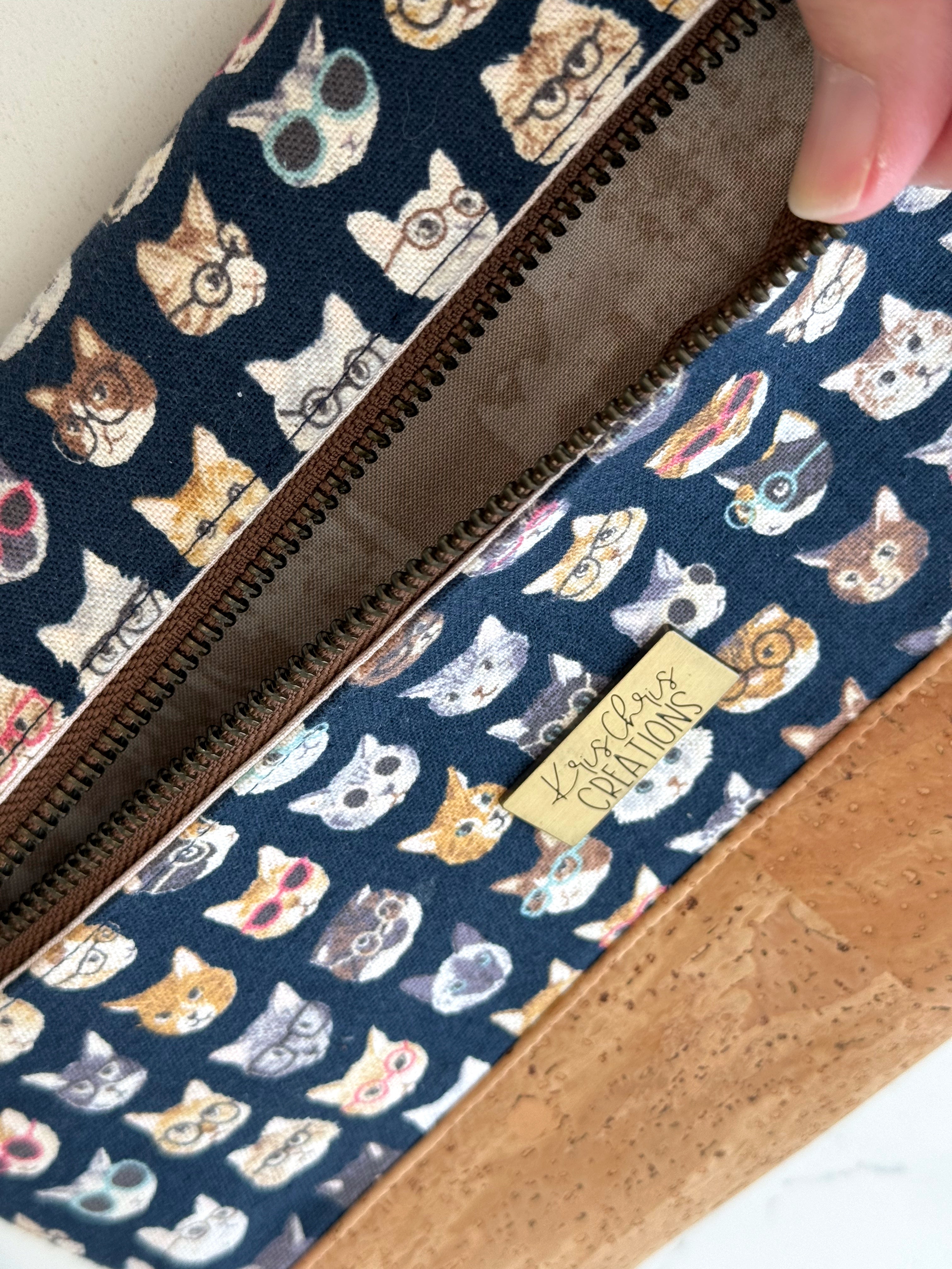 Rear pocket of cats in glasses clutch bag opens with a zipper to show textured brown interior fabric. 