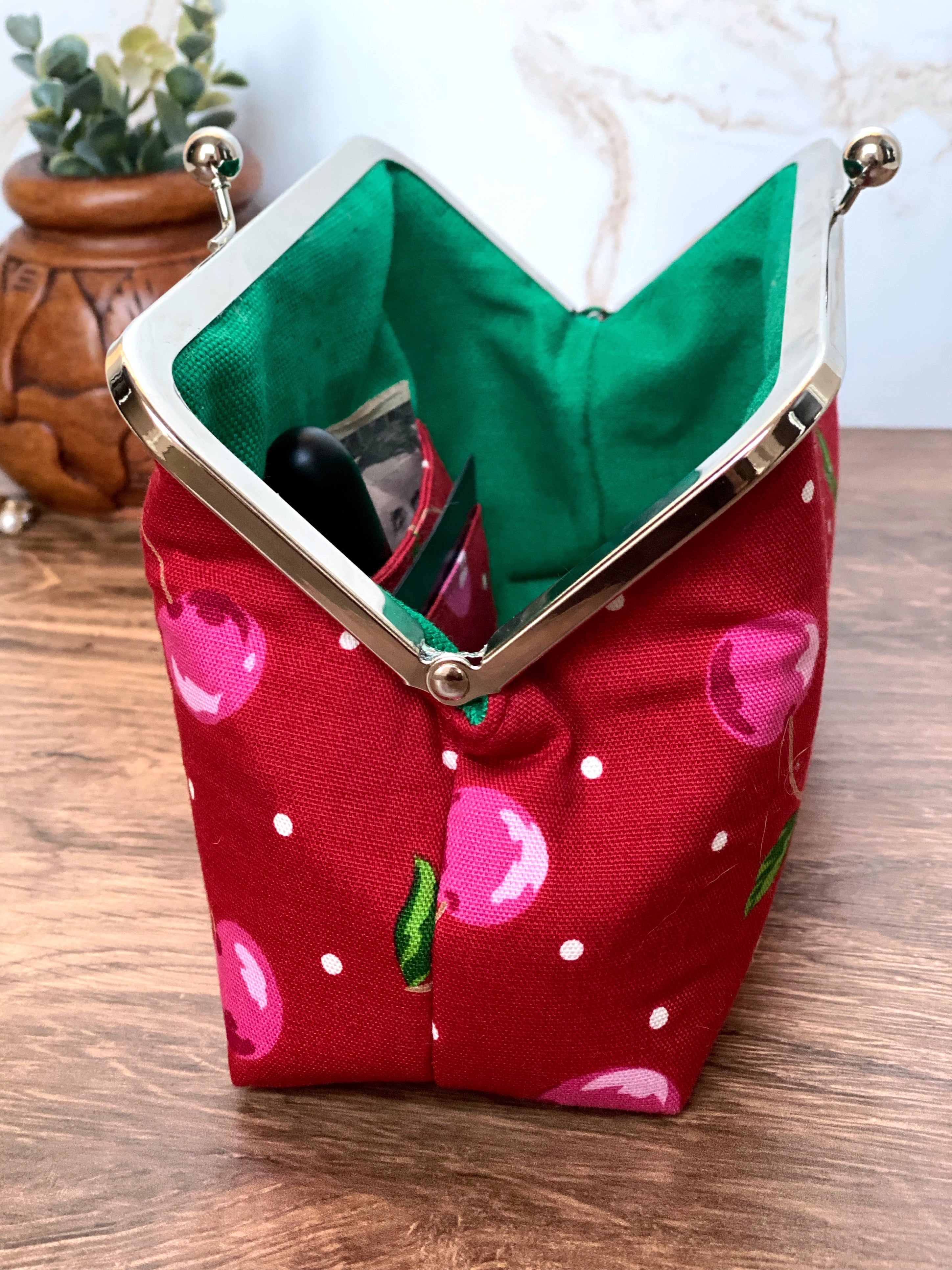 Side view of opened cherry clutch shows bright green canvas lining and interior pocket for cash and cards